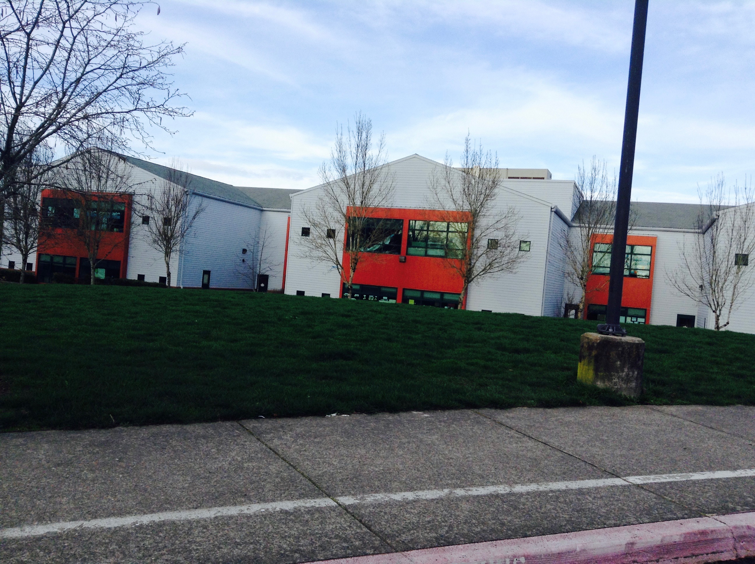 Two-story school building with white and orange exterior on a grassy hillside.