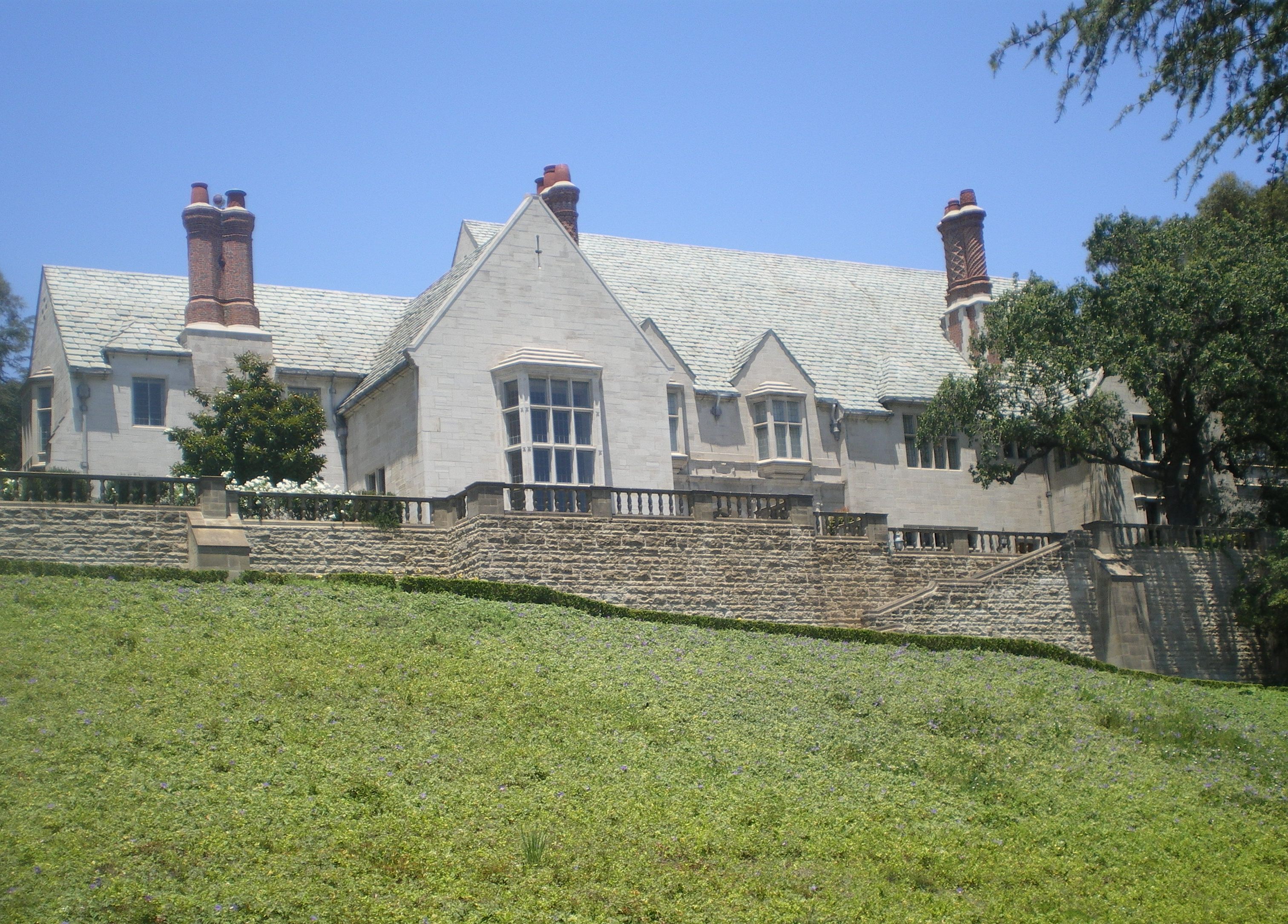 Stone mansion with slate roof and green lawn under a clear blue sky.