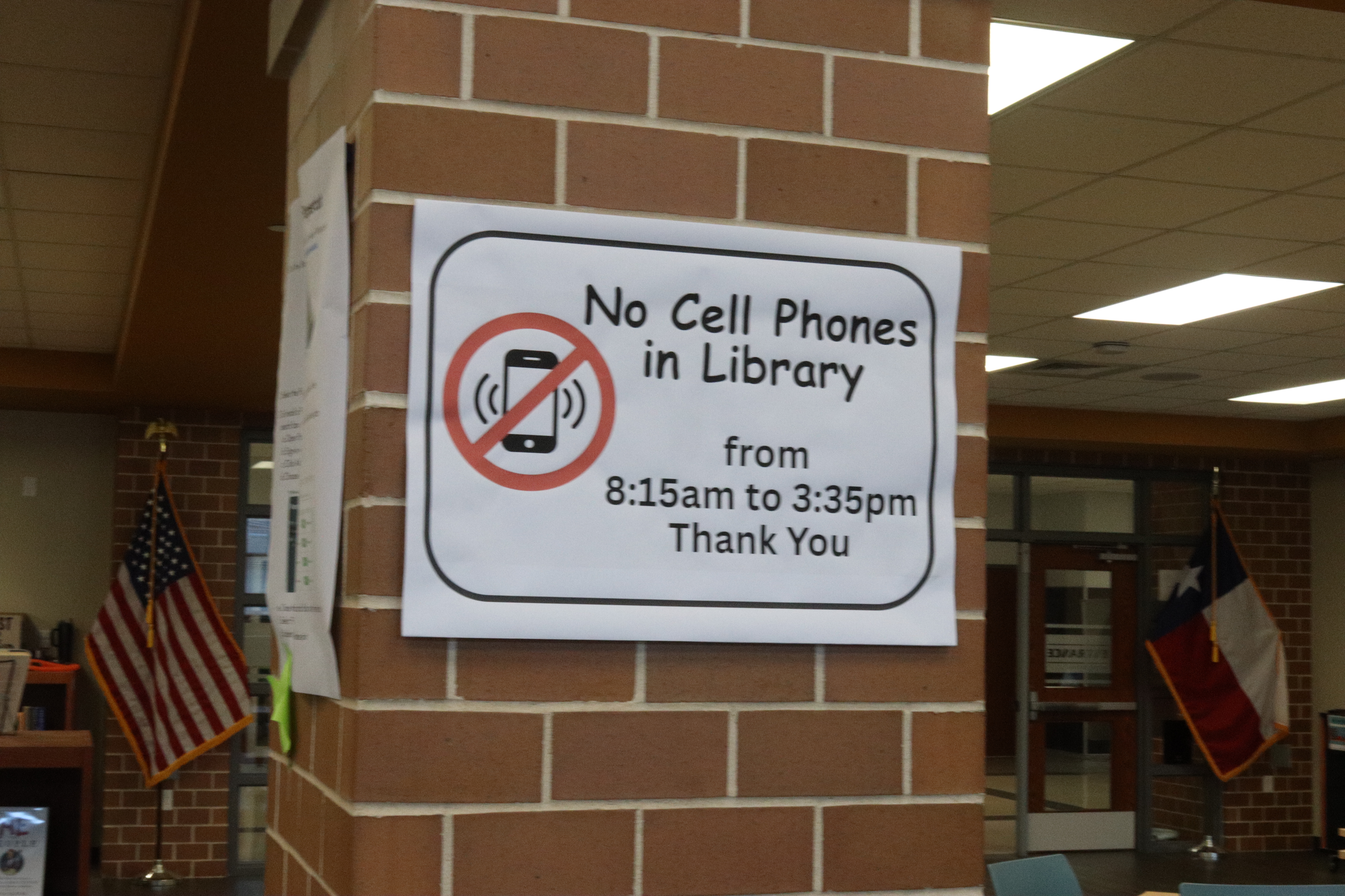 A printed sign on a brick column showing a crossed-out cell phone icon.