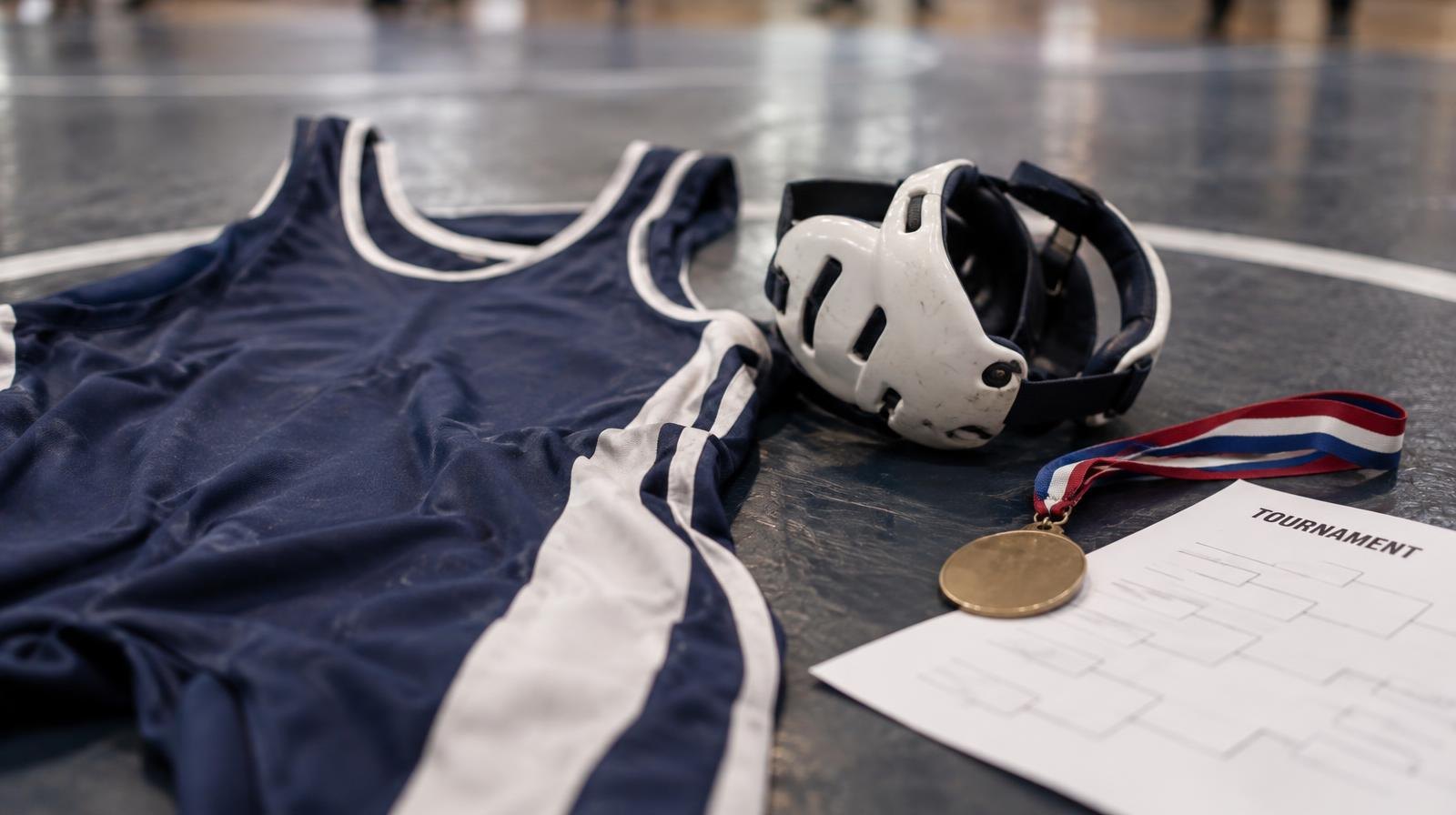A wrestling singlet and headgear laid on a mat next to a championship medal.
