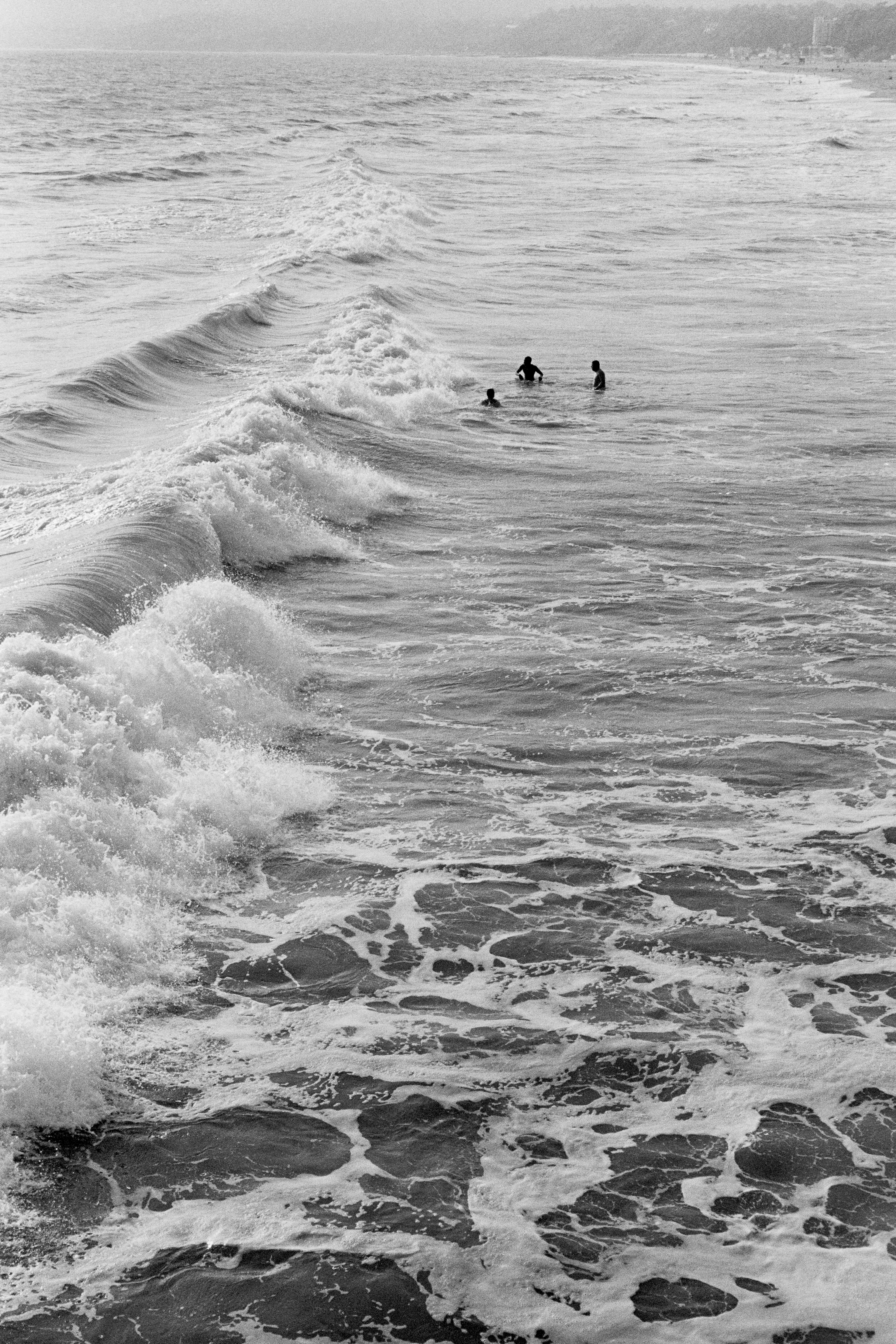 Swimmers in churning ocean surf with large breaking waves in the foreground.