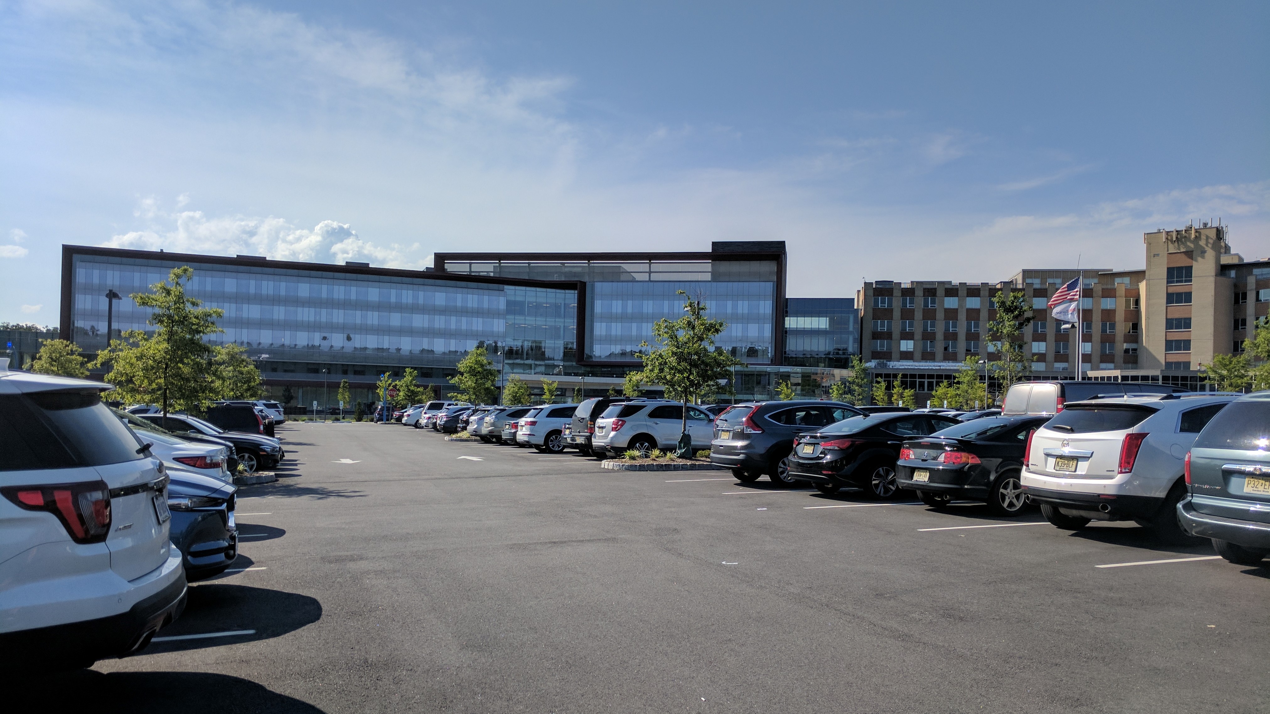 Large modern glass-and-steel hospital building with a full parking lot in front.