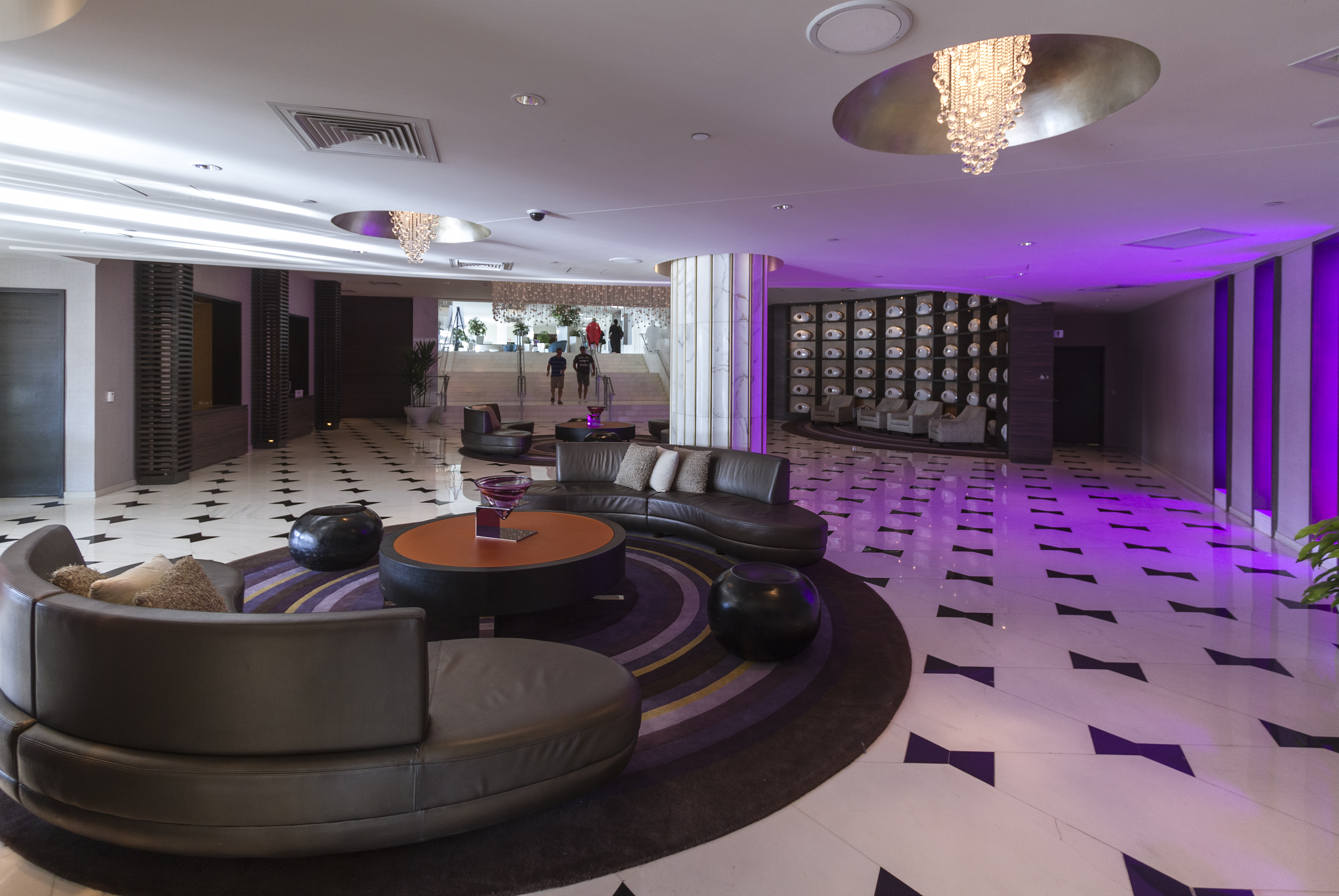 Upscale hotel lounge with curved dark leather sofas, geometric tile flooring, and purple ambient lighting.