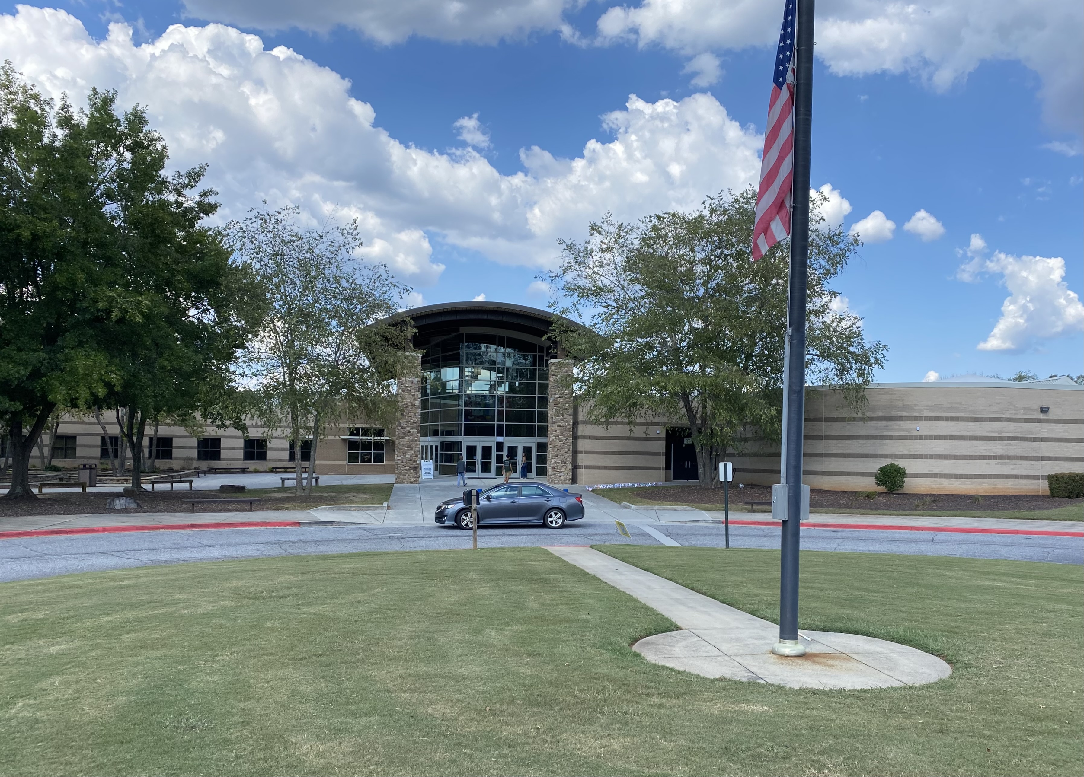 Front exterior of a school building with stone facade, arched glass entrance, and American flag.