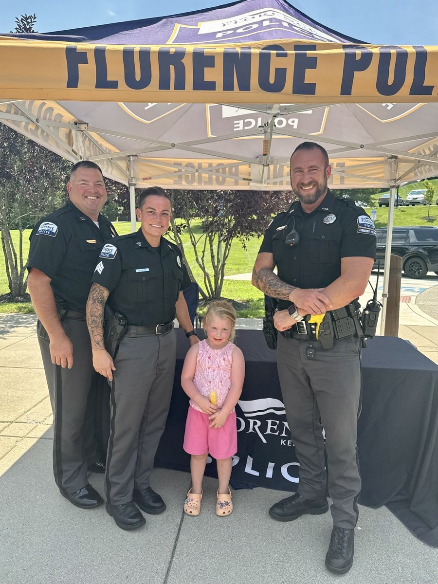 Three police officers and a young child pose under a Florence Police canopy tent outdoors.