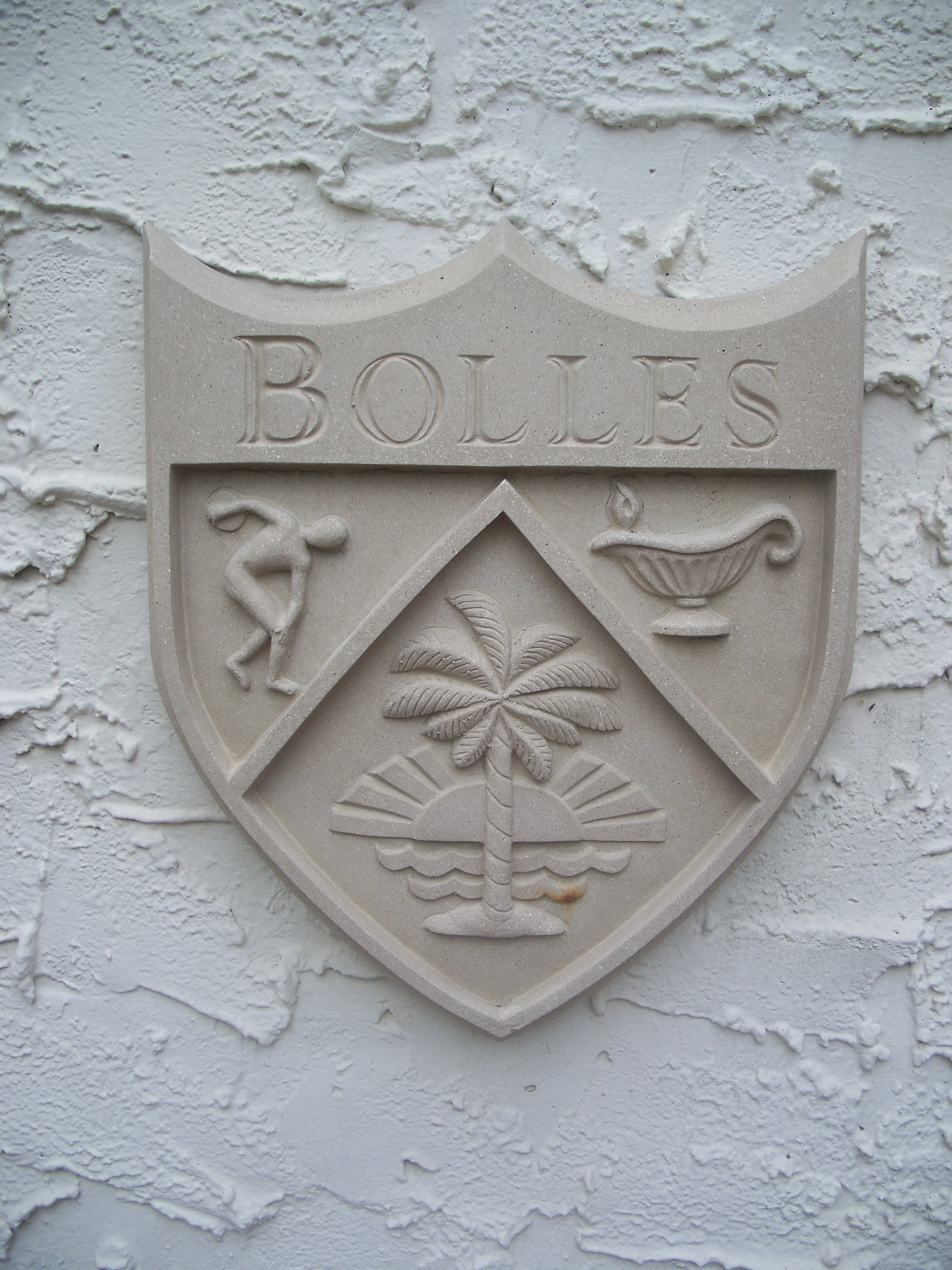 Stone-carved school crest with shield design mounted on a white stucco wall.