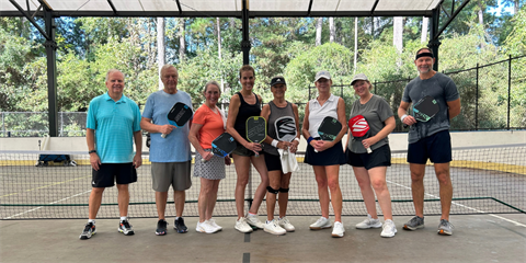Group of adults holding pickleball paddles on a covered outdoor court.