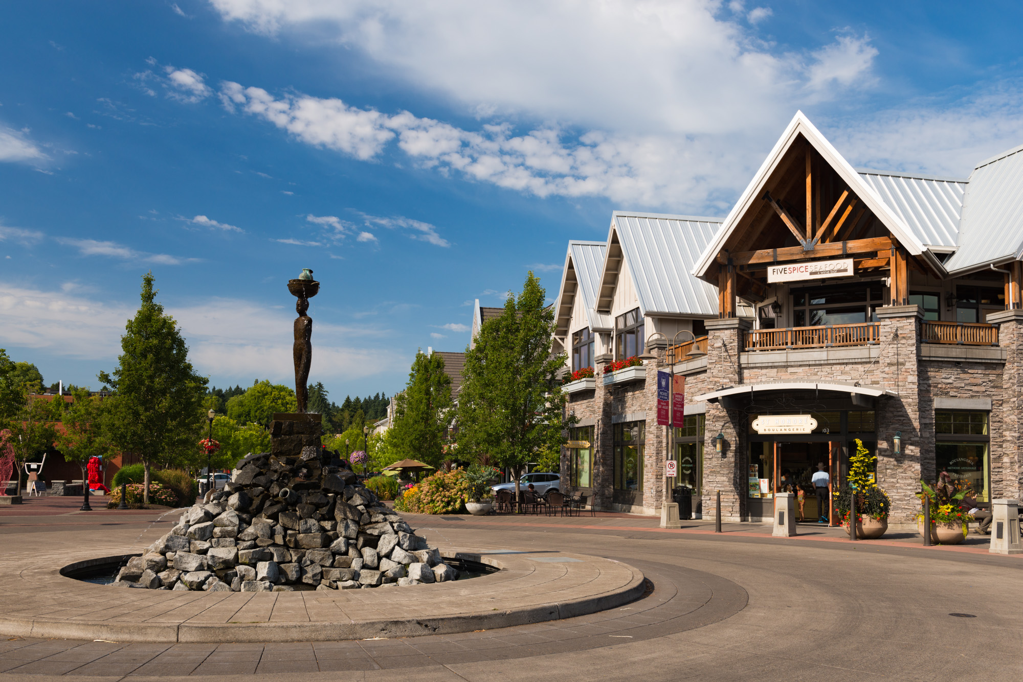 Abstract rock sculpture in a downtown plaza surrounded by stone-clad buildings and evergreen trees.