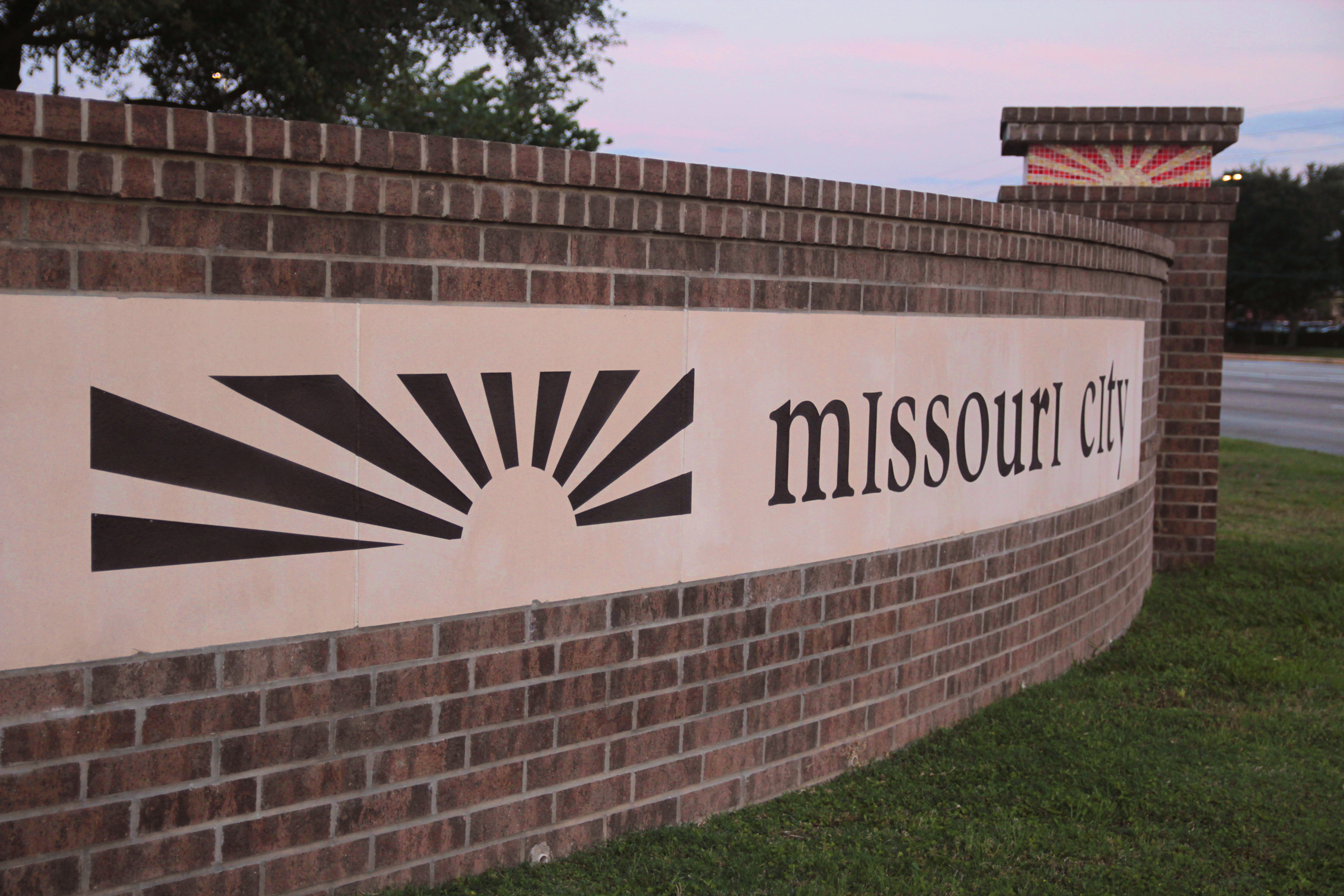 Brick entrance sign for Missouri City, Texas, lit at dusk near a major intersection.