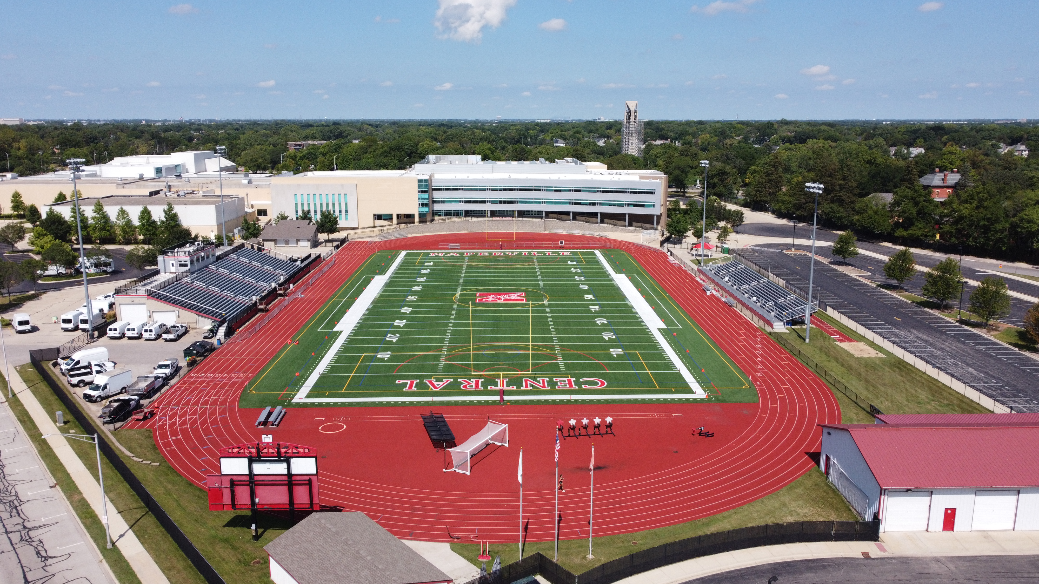 Aerial view of a high school football stadium with red track and school building behind.