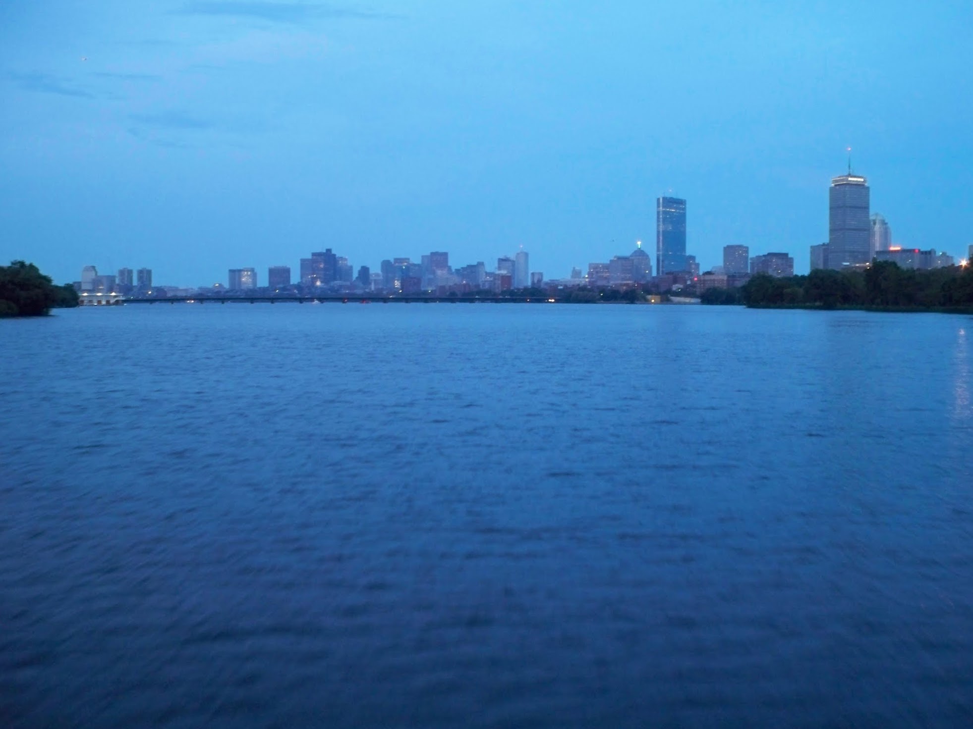Calm river water at dusk with a city skyline and bridge visible in the distance.