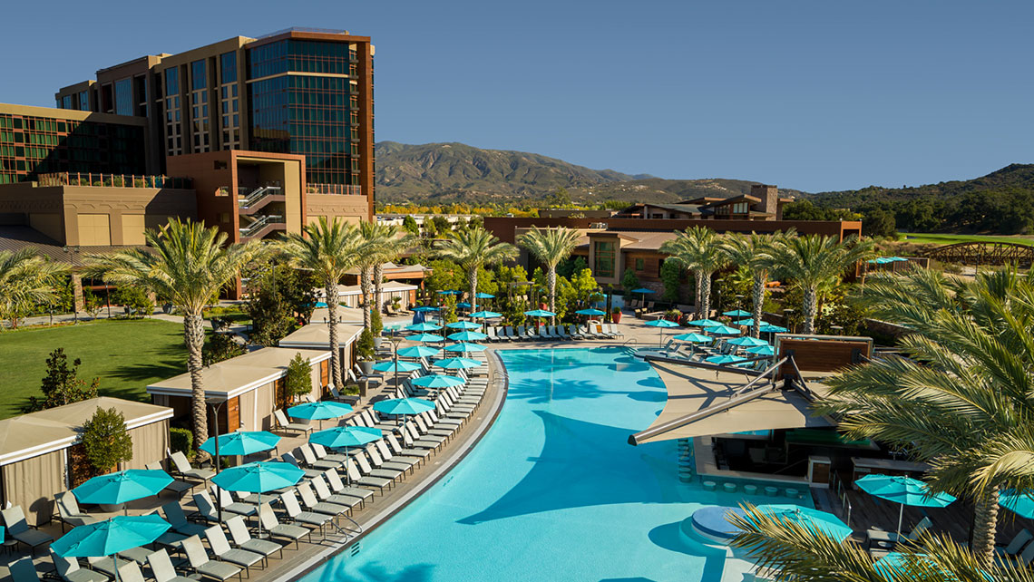 Aerial view of a large resort hotel with a turquoise lagoon pool and palm trees.