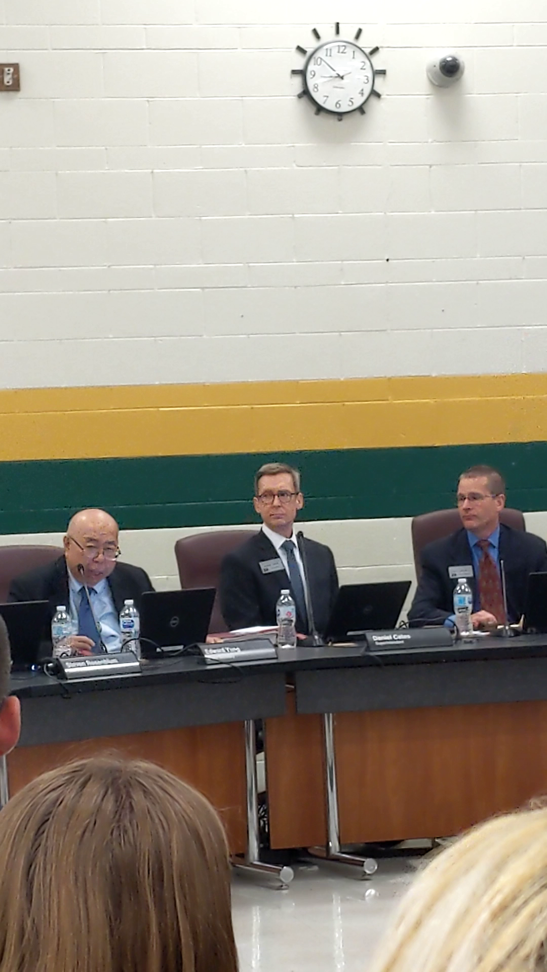 Three men in business attire seated at a school board panel table with nameplates.