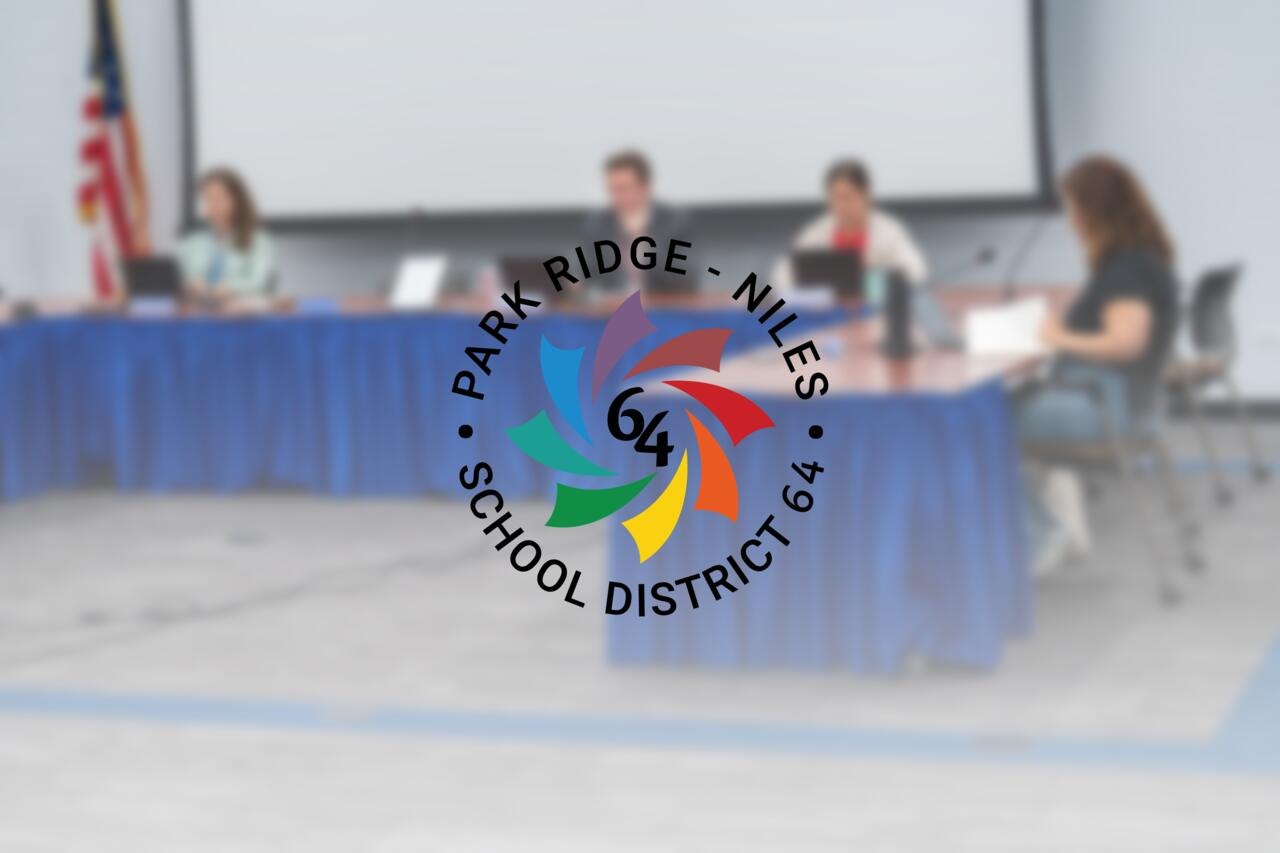 Several people seated at a blue-draped table in a school board meeting room with a projection screen.