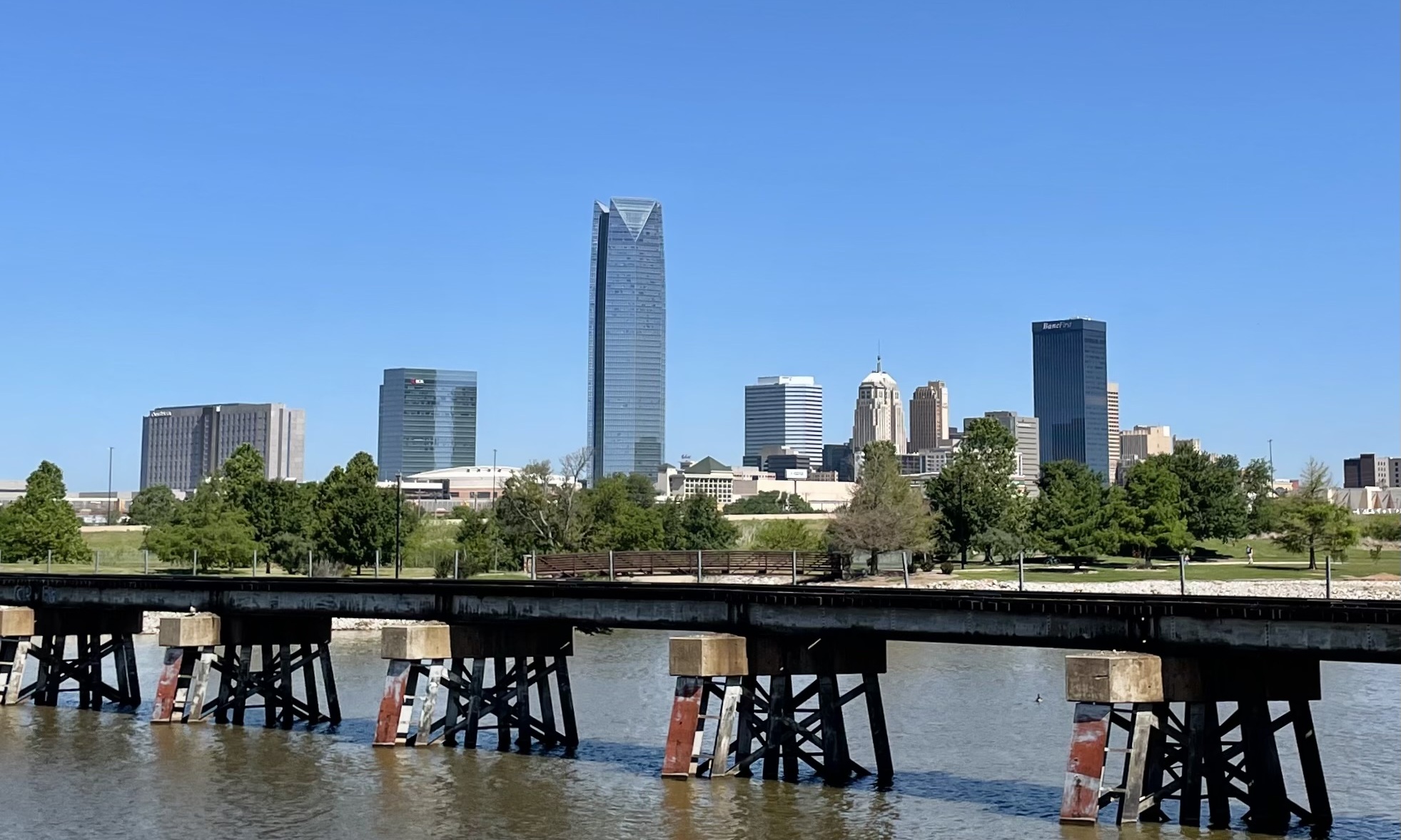 Modern downtown skyline reflected across a river with a wooden pier in the foreground.