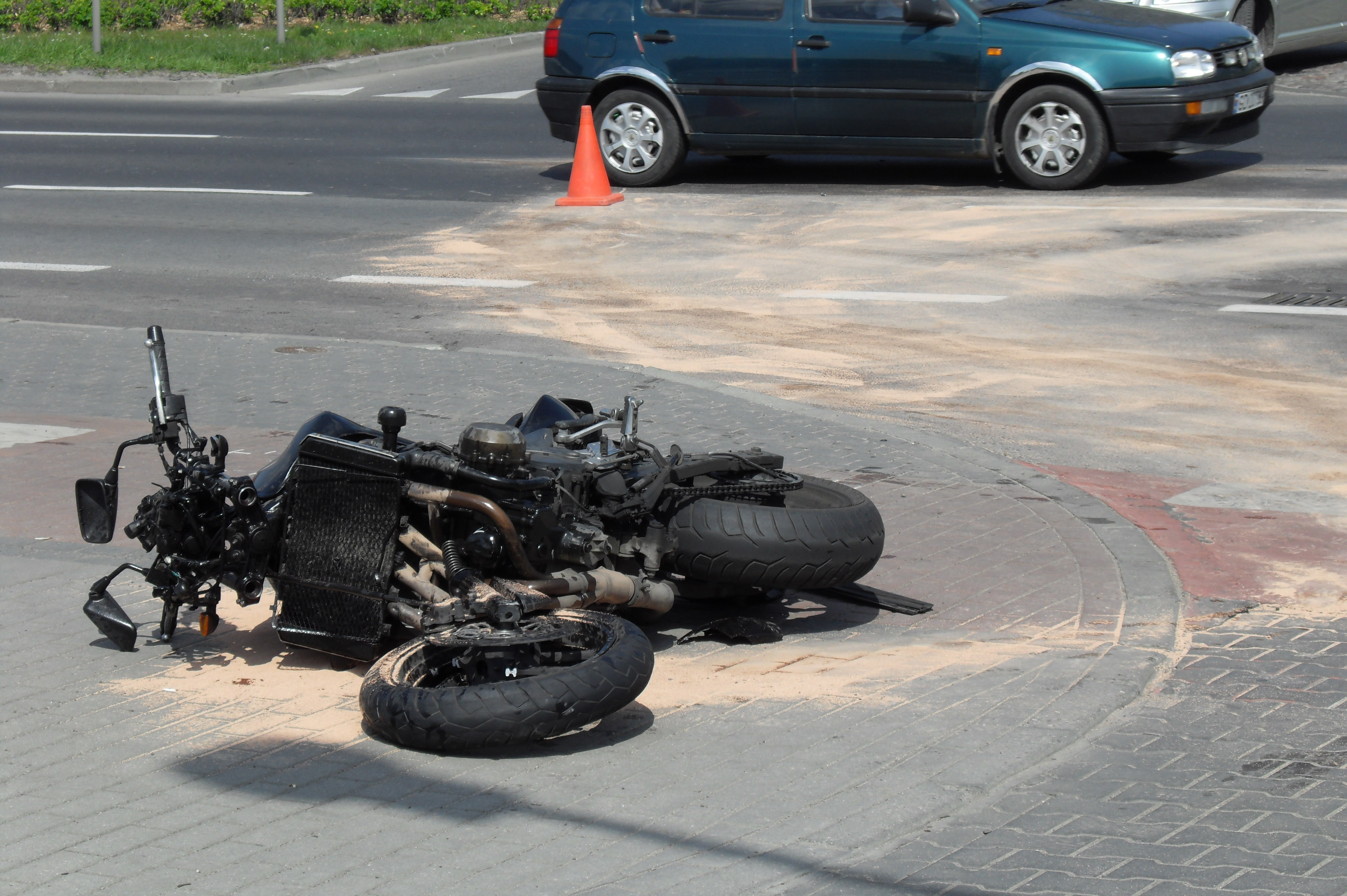 A heavily damaged motorcycle lying on its side at a road intersection with a traffic cone nearby.