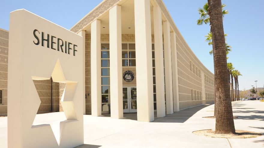 Government building exterior with a large Sheriff sign, white columns, and palm trees.
