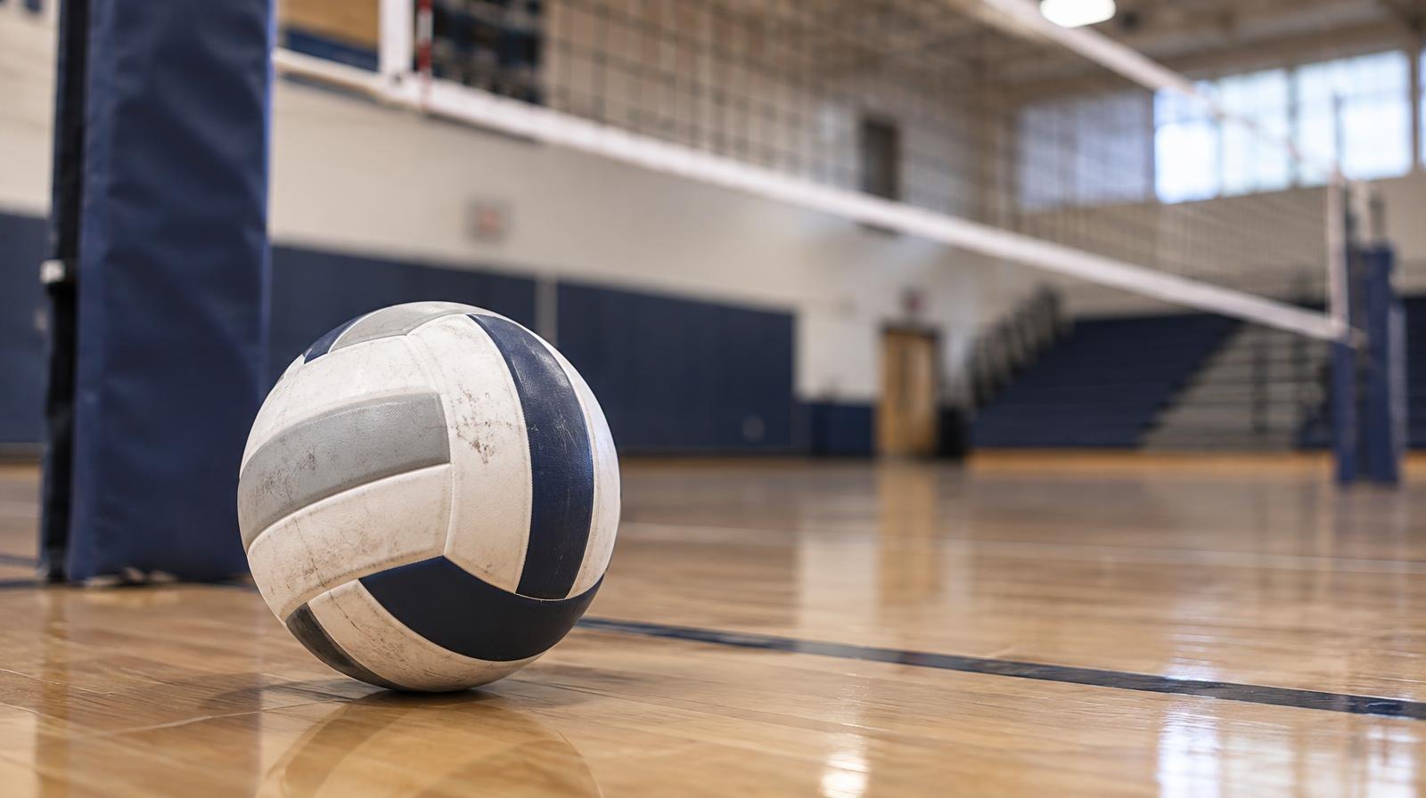 A volleyball resting on a hardwood gym floor near a net post.