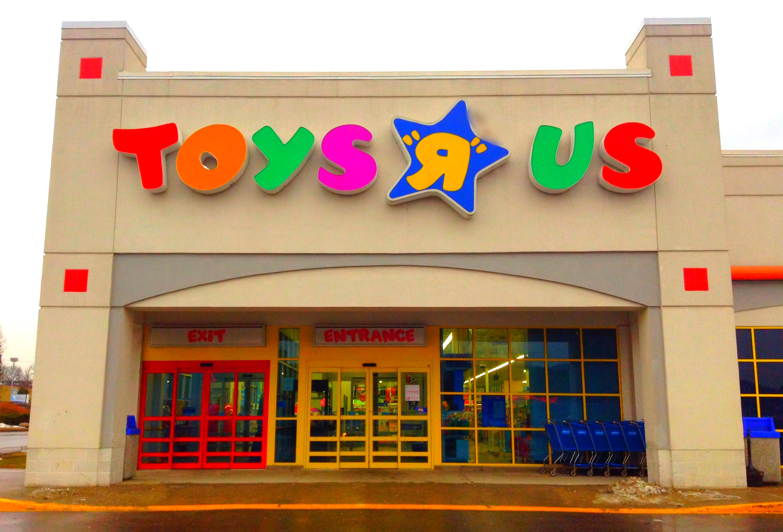 Exterior of a Toys R Us store with colorful logo signage and shopping carts near the entrance.