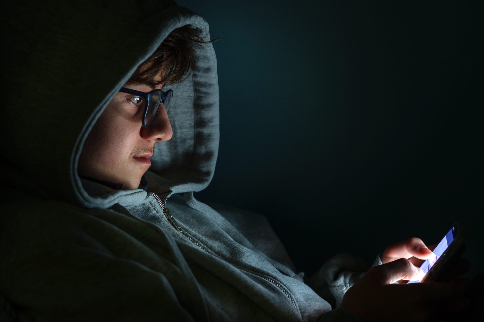 Teenager using glowing smartphone in dark room