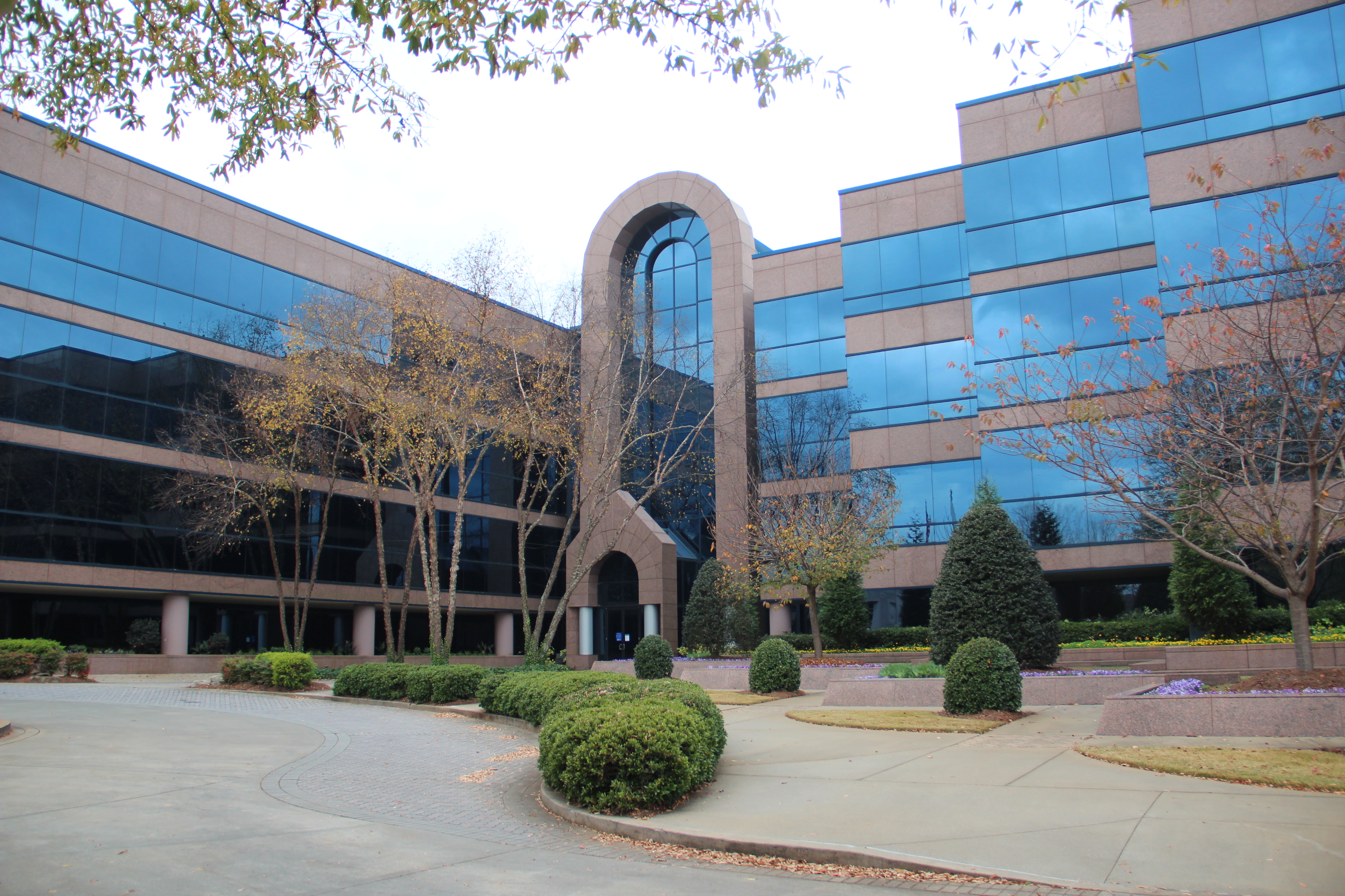 Multi-story office building with blue reflective glass facade and brick arched entryway, landscaped grounds.