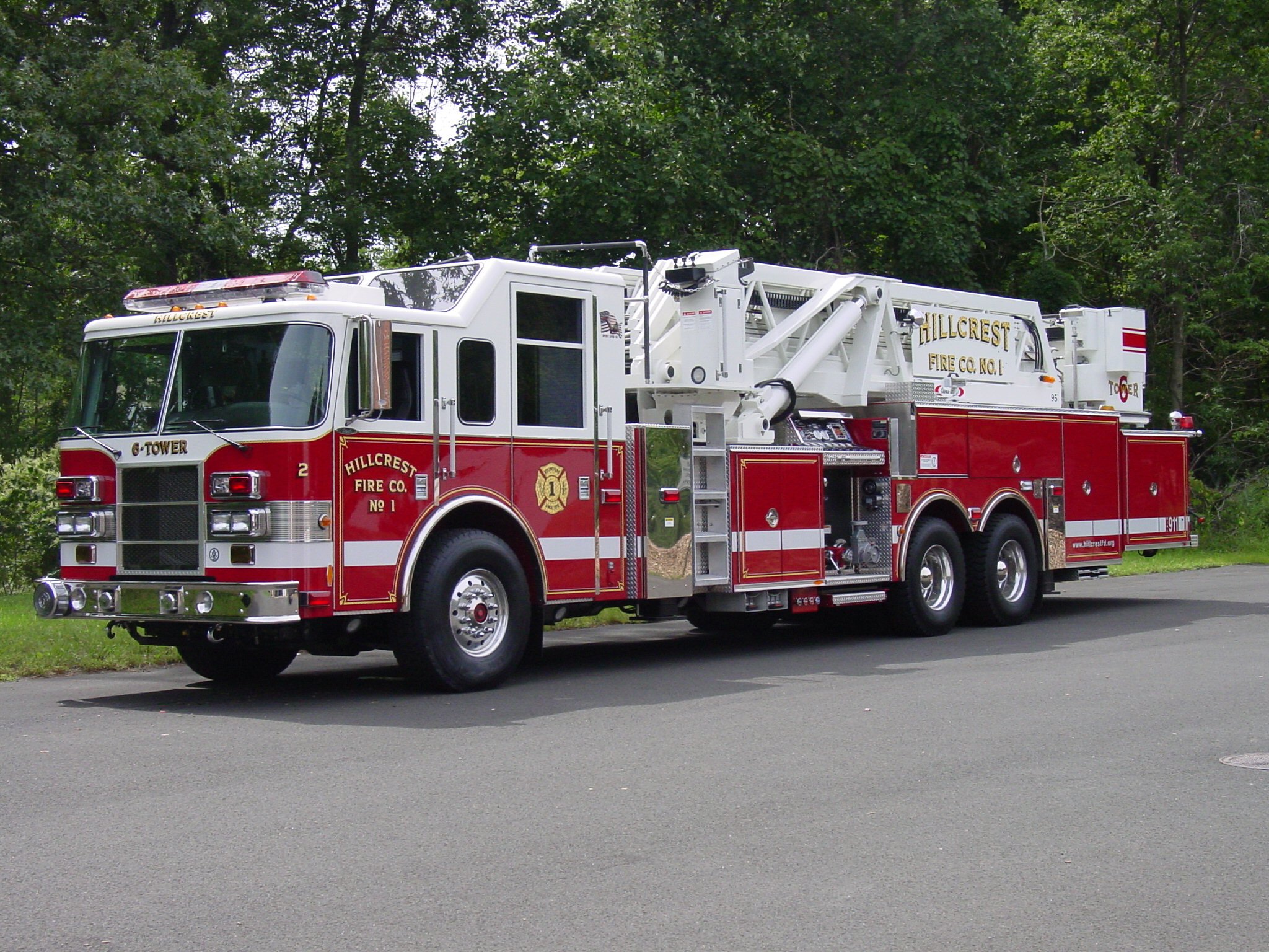 A large red aerial platform fire truck parked on a road with trees in the background.