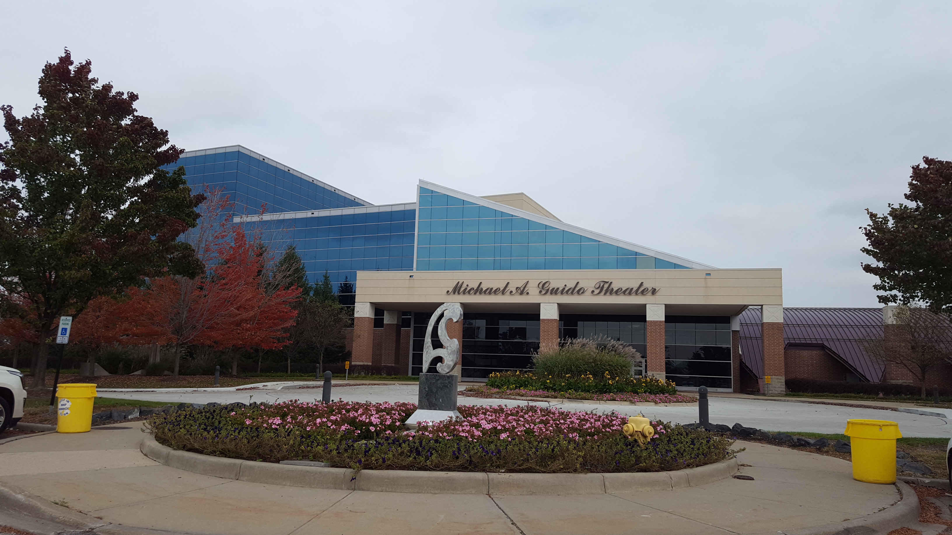 Exterior of a performing arts center with a circular landscaped roundabout and glass pyramid structure behind the entrance.