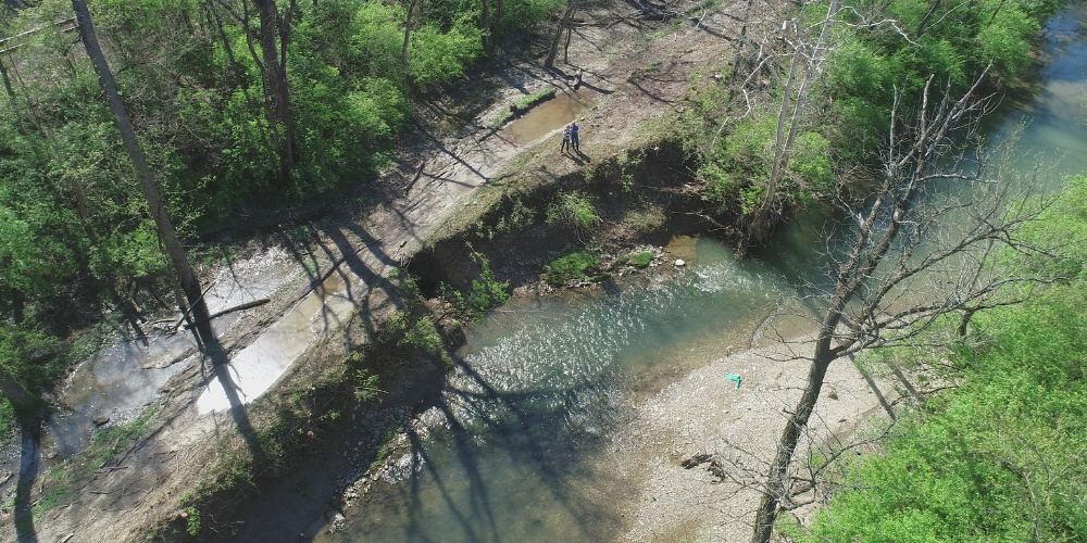 Aerial view of a creek with eroded banks, exposed sediment, and surrounding trees.