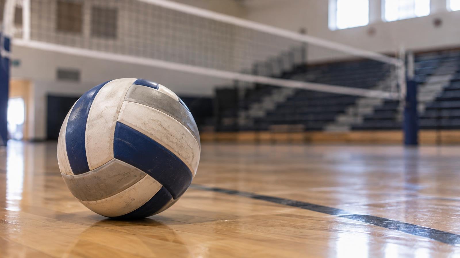 A volleyball resting on a hardwood gymnasium floor near a net.