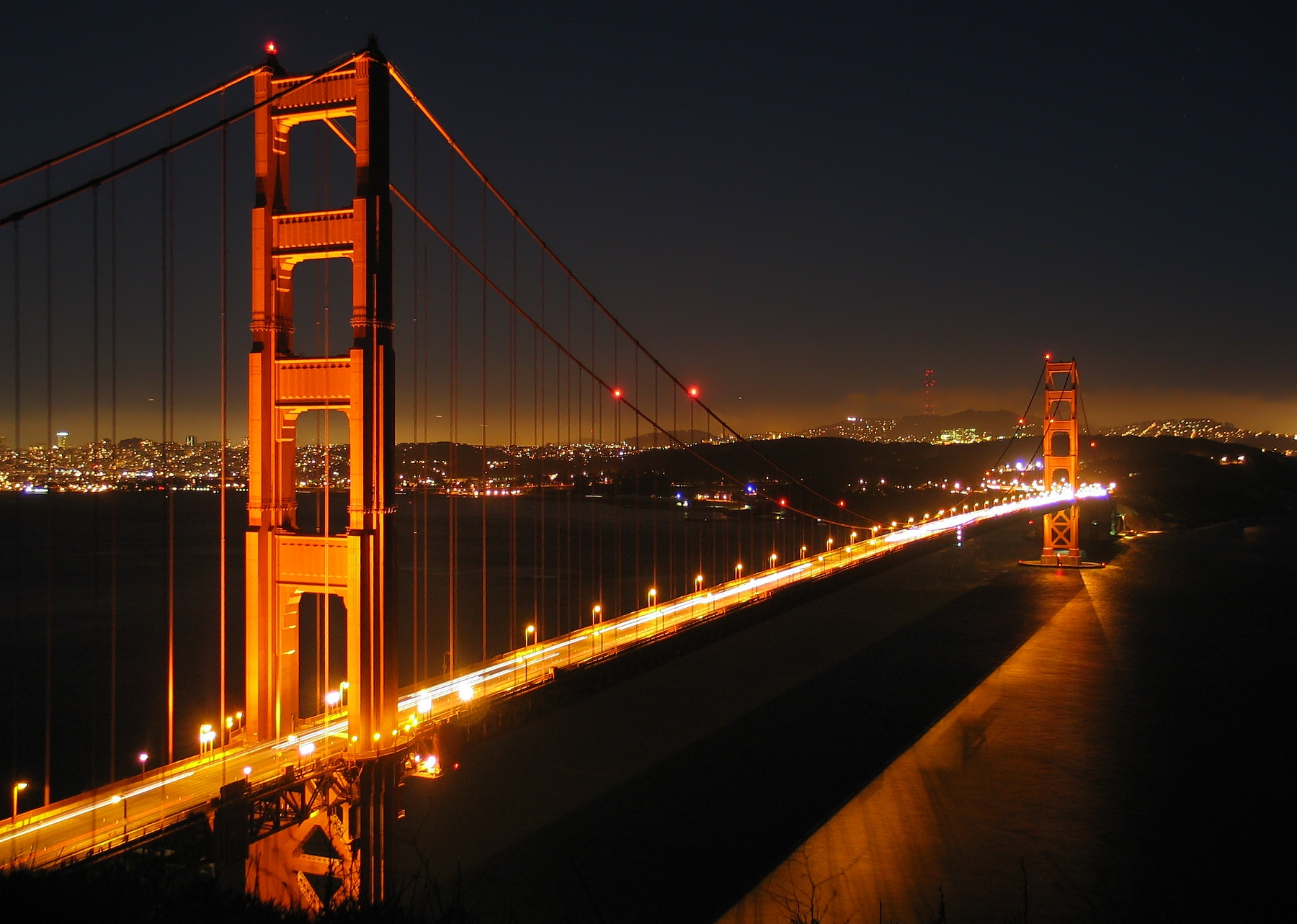 Golden Gate Bridge lit at night with light trails from traffic on the roadway.