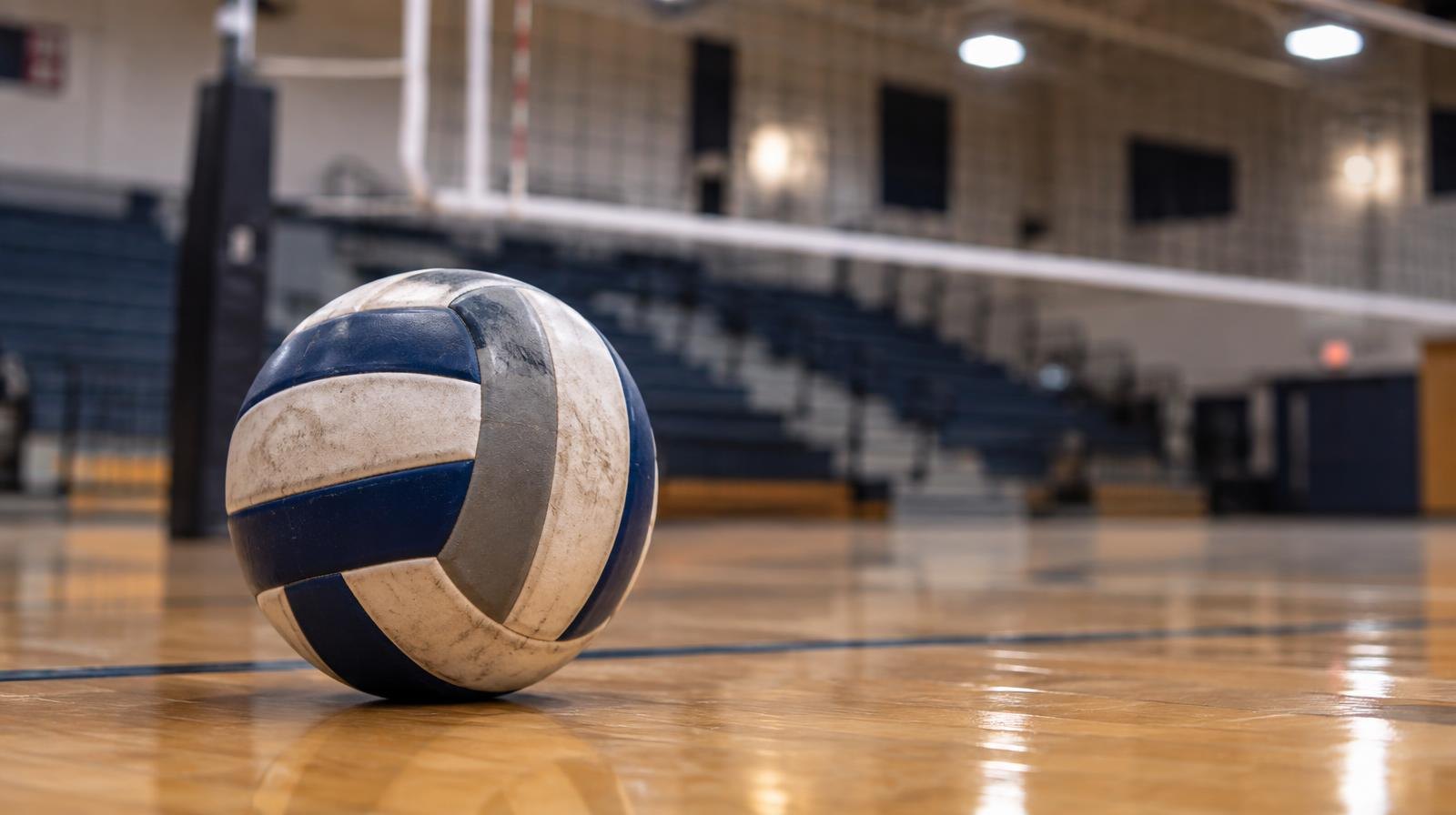 A volleyball resting on a hardwood gymnasium floor near a net.