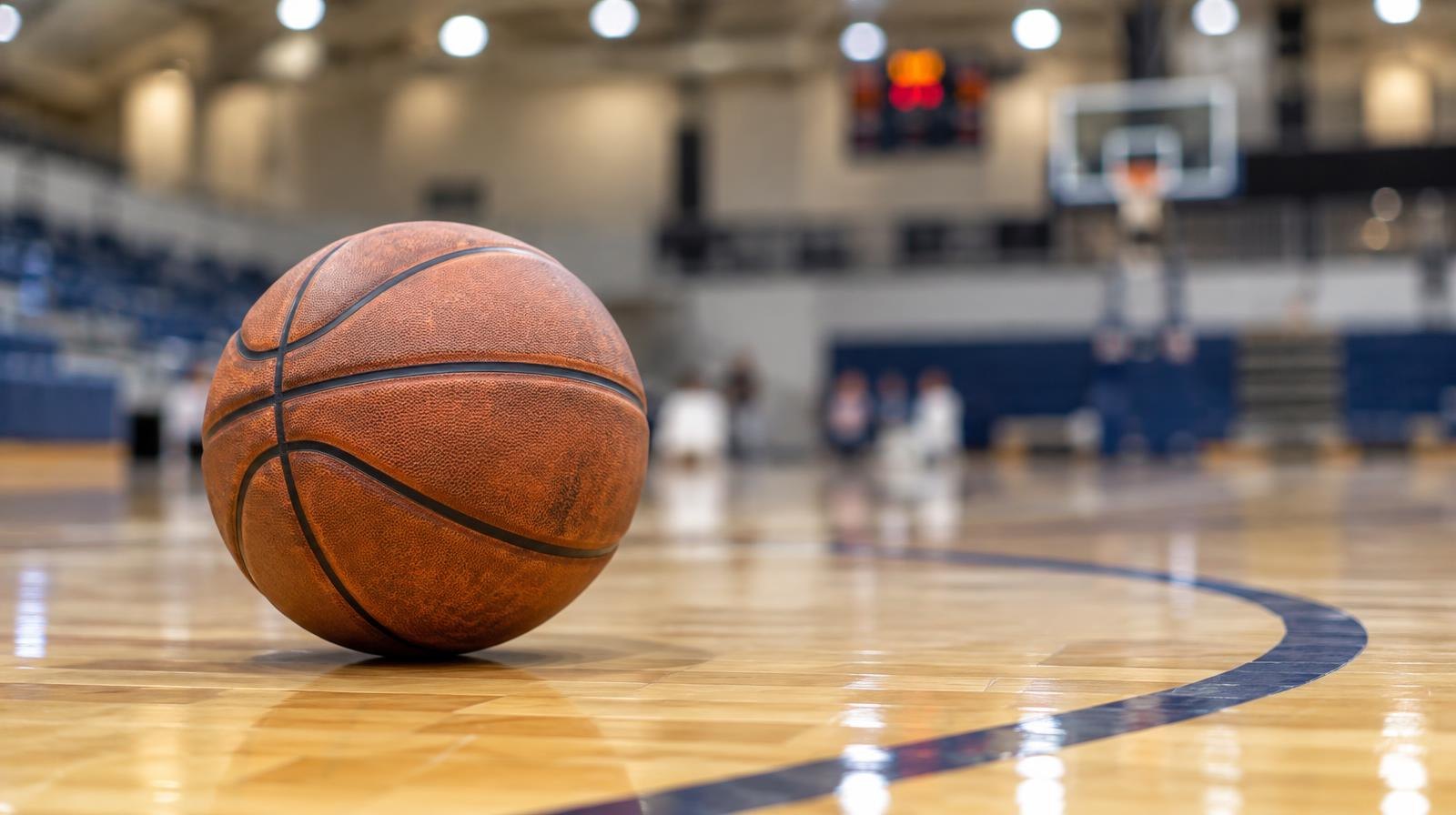 A basketball resting on a hardwood court near a painted arc line.
