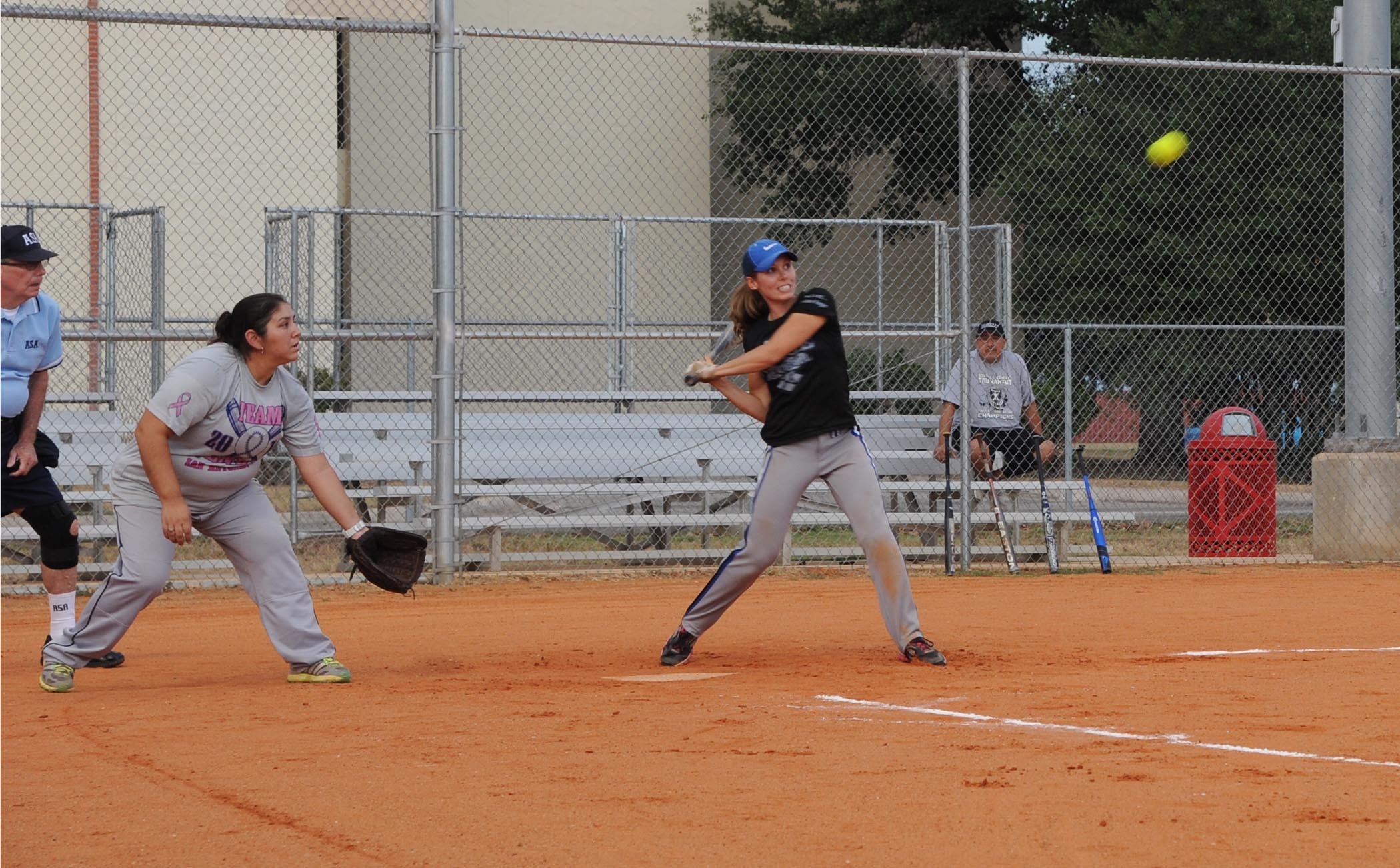 A female softball player swings a bat during a scrimmage with an umpire in blue behind the plate.