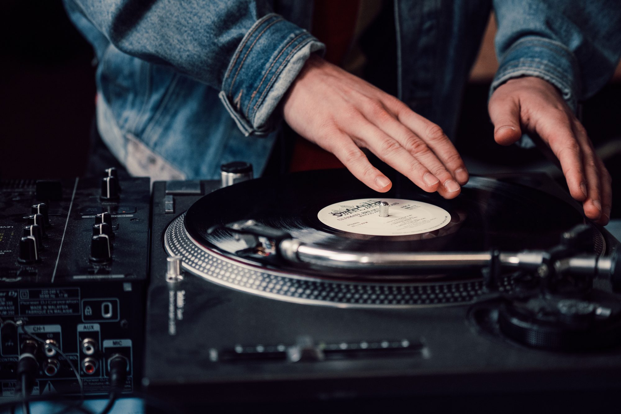 DJ mixing vinyl records on a turntable, creating live music with a sound mixer.