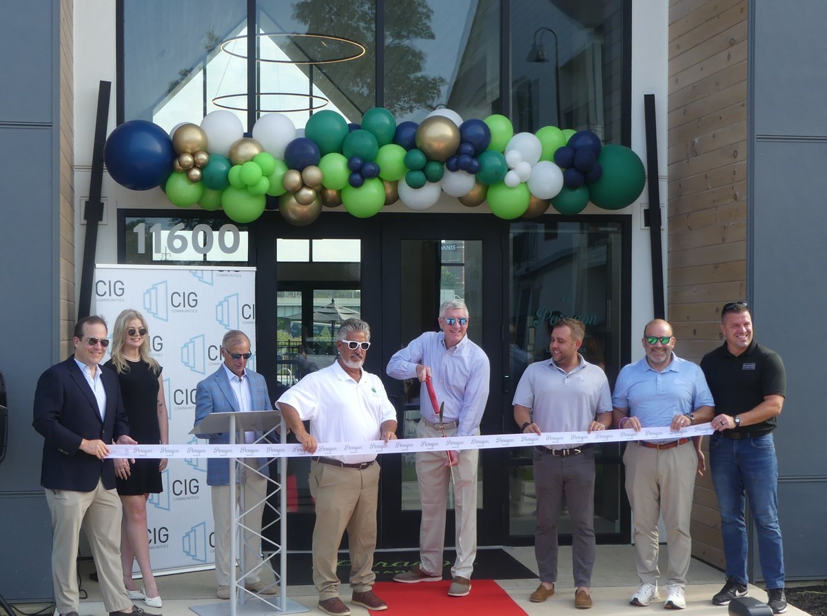 Group of people holding a ribbon in front of a building entrance decorated with a balloon arch.
