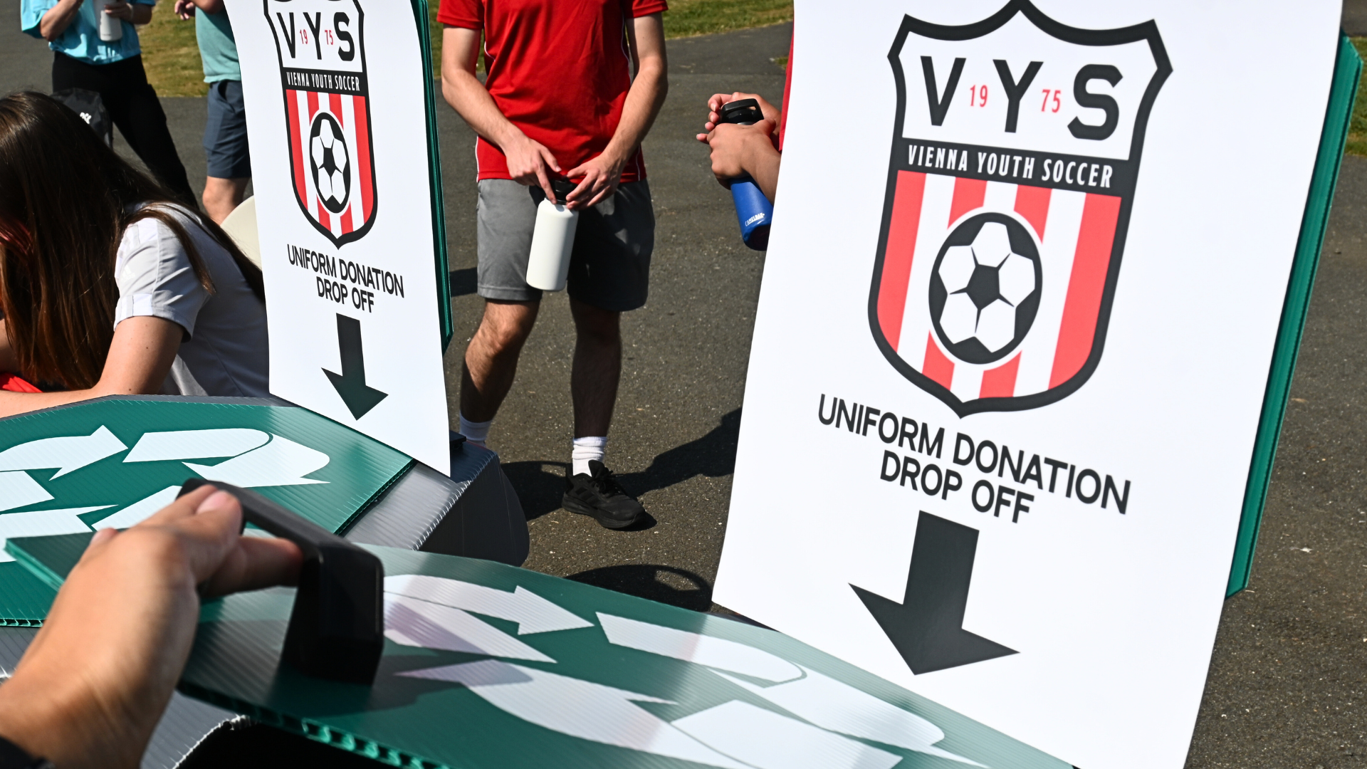 Two large green donation bins with VYS logos and uniform drop-off signs at an outdoor event.