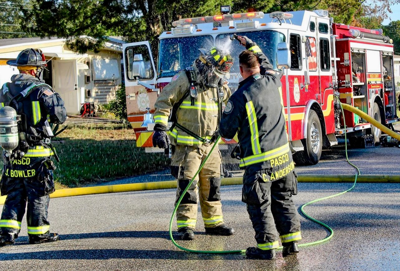 Three firefighters in turnout gear performing a decontamination procedure at a fire scene.