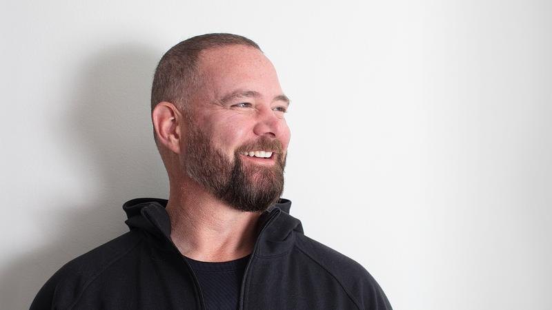 Smiling man with buzz cut and trimmed beard wearing a black zip-up jacket.