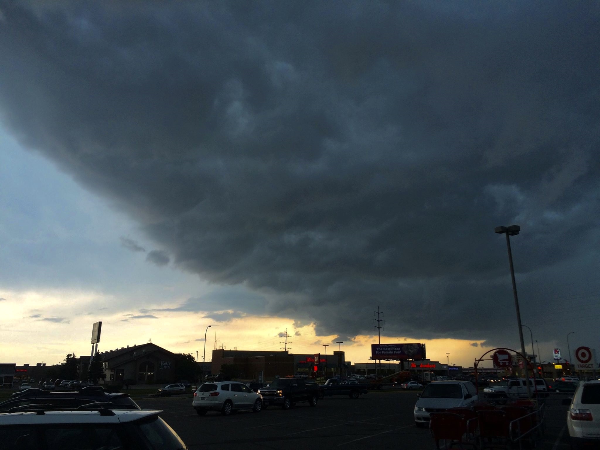 Dark storm clouds roll over a commercial parking lot at dusk.