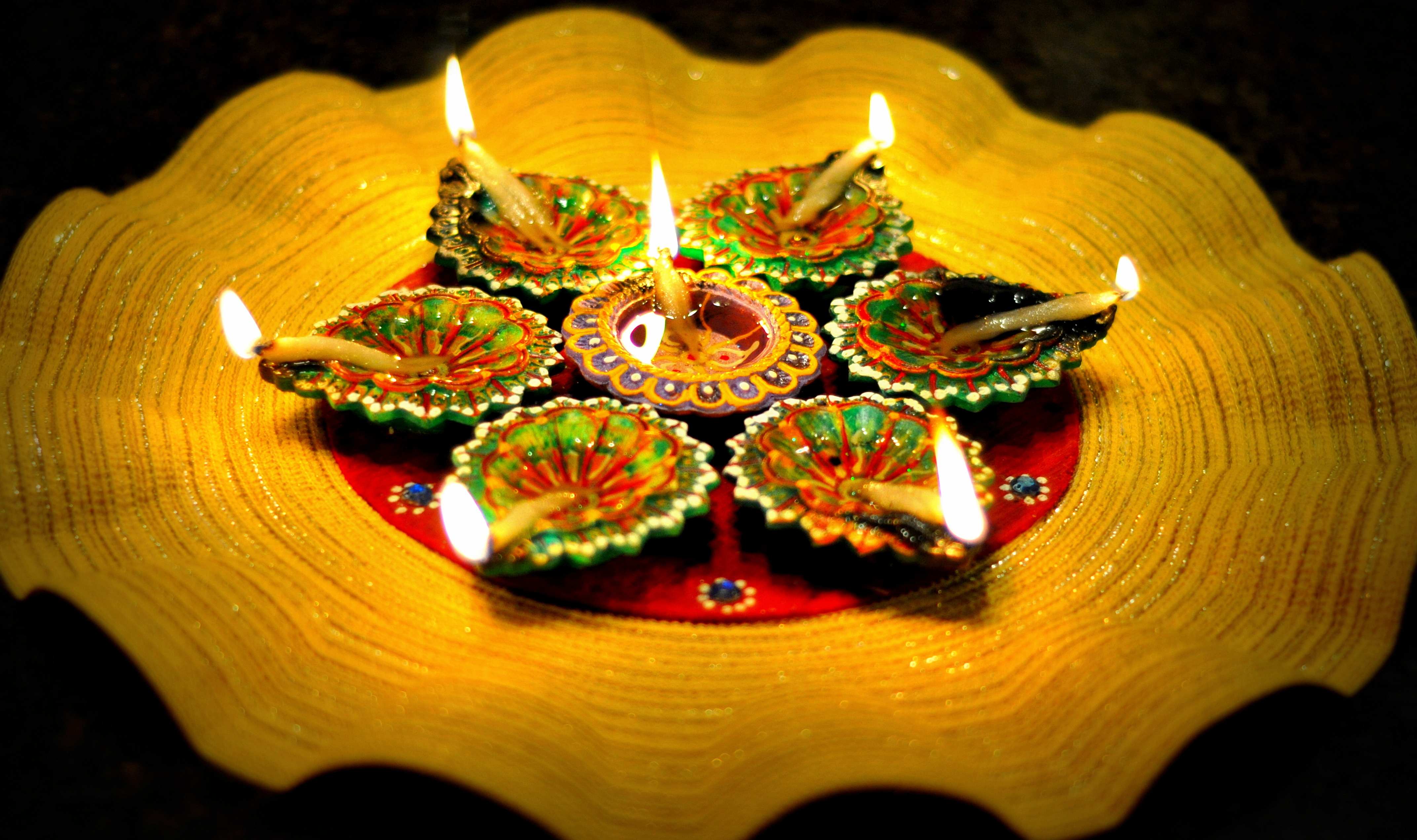Seven lit clay diya oil lamps arranged in a circle on a gold decorative plate.