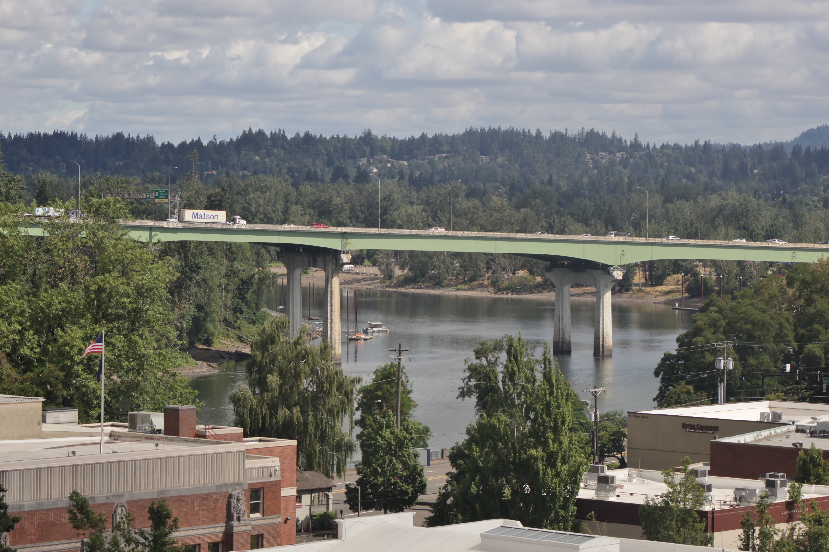 Green concrete highway bridge spanning a wide river, forested hills in the background.