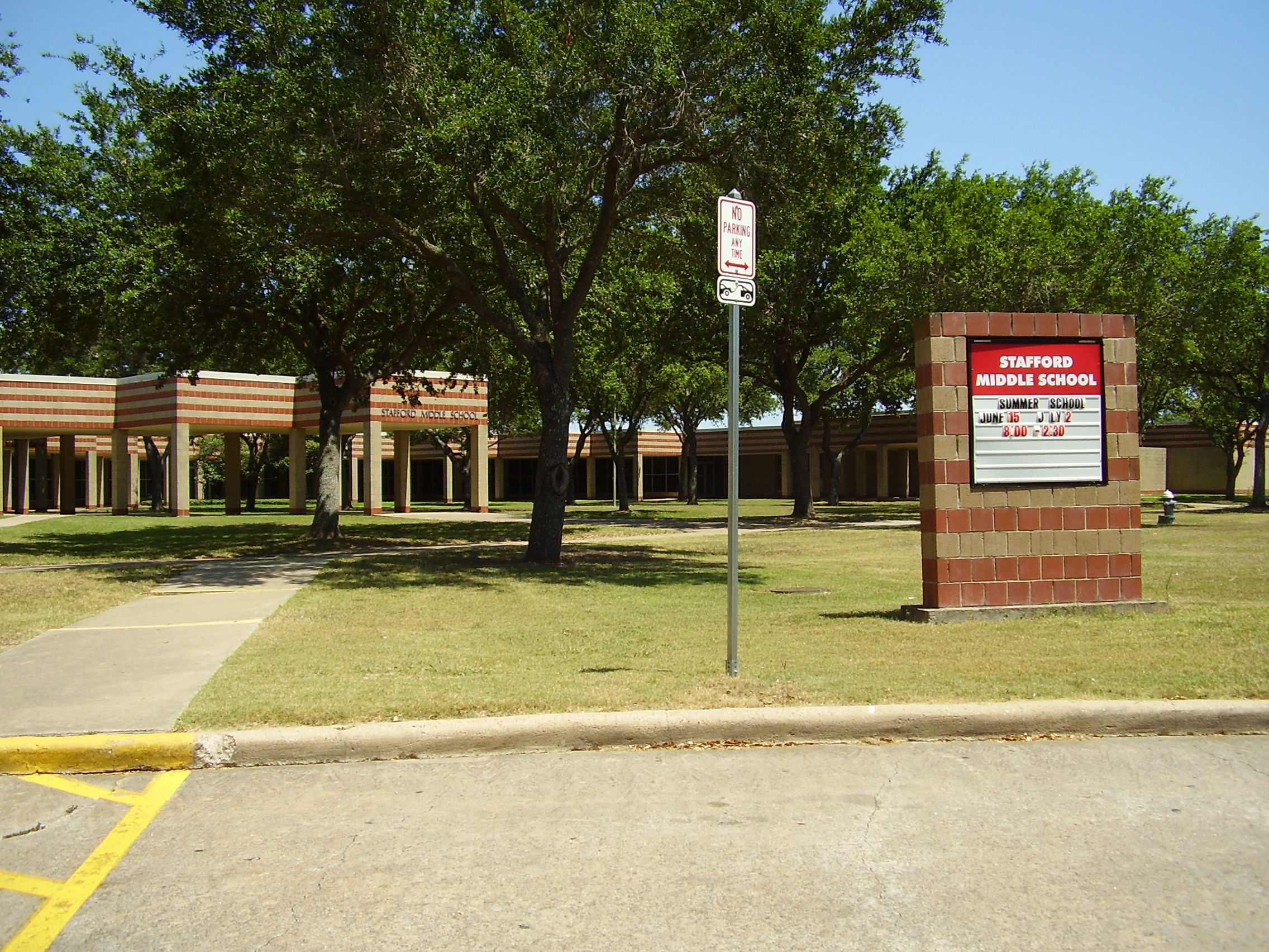 Single-story brick school building with a marquee sign and shade trees.