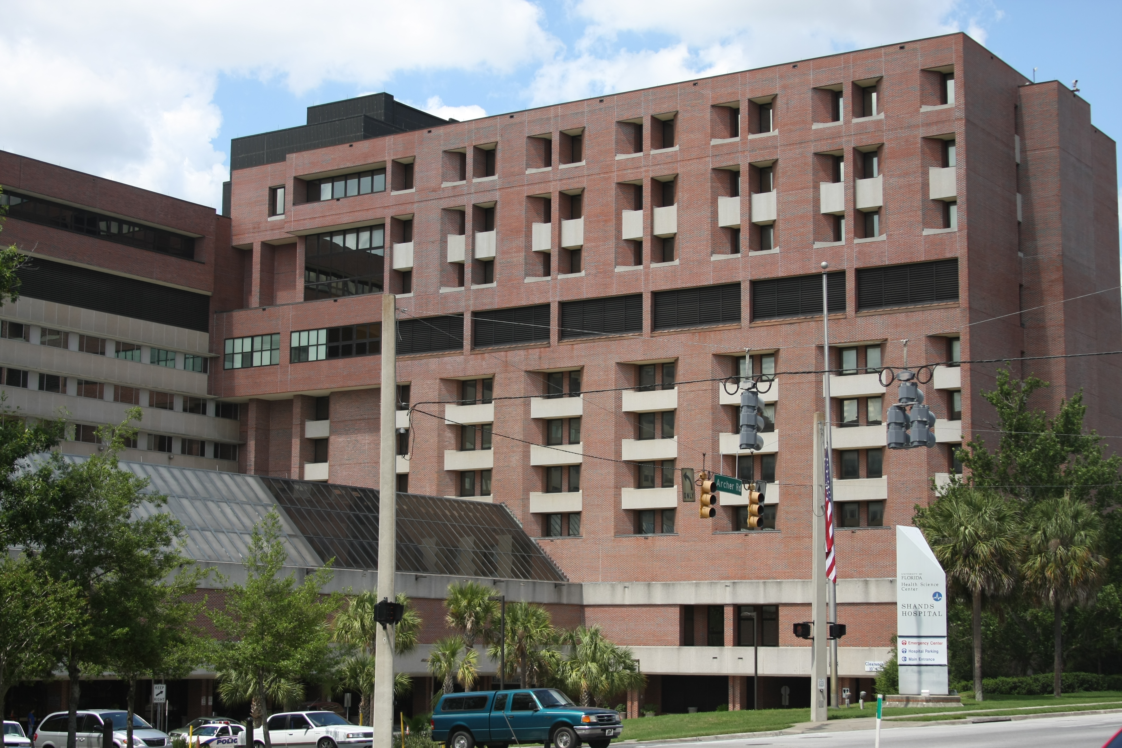 Multi-story red brick hospital building with an American flag and palm trees out front.