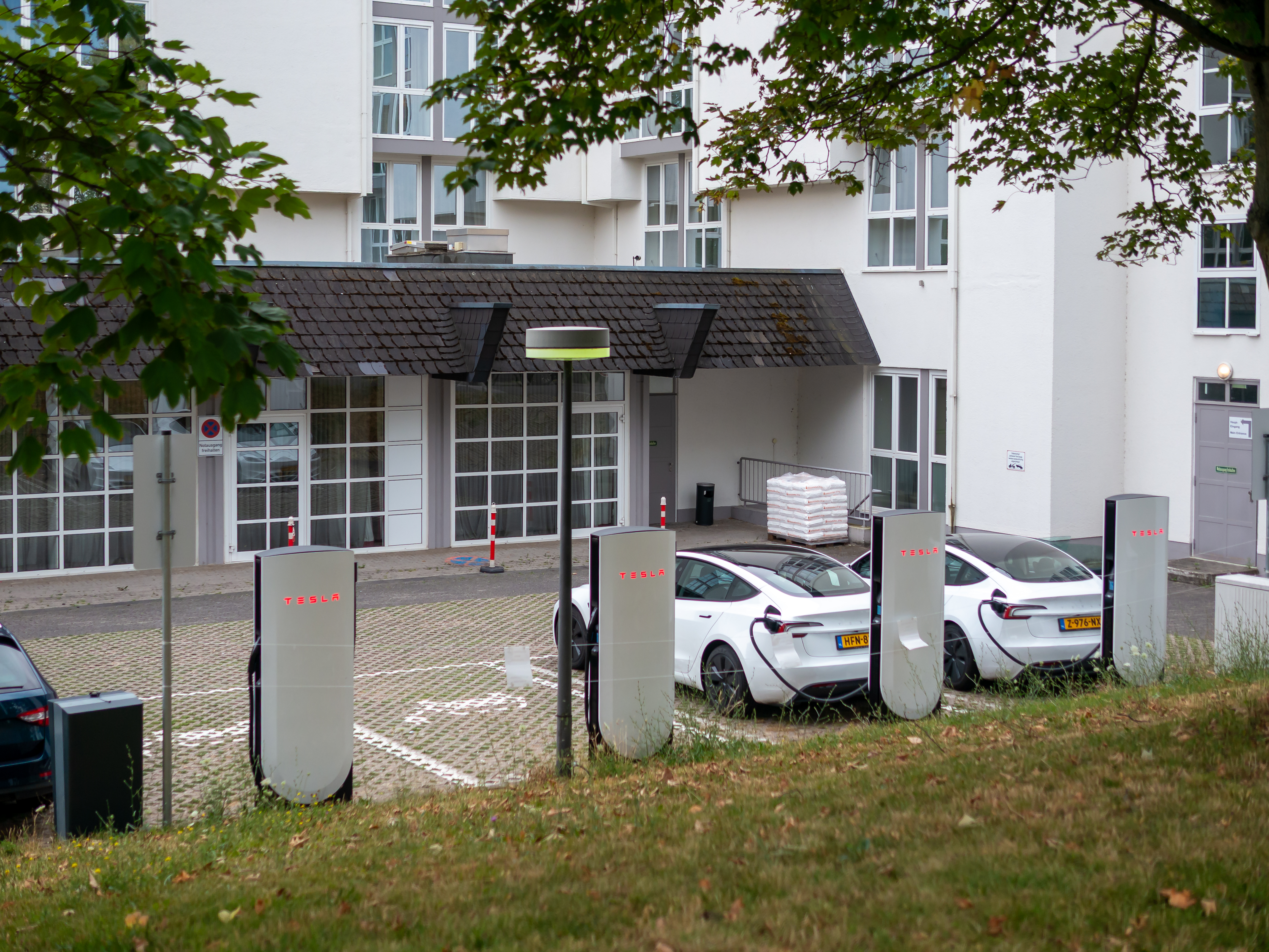 Several Tesla V4 Supercharger pedestals in a parking lot with two white electric vehicles charging.