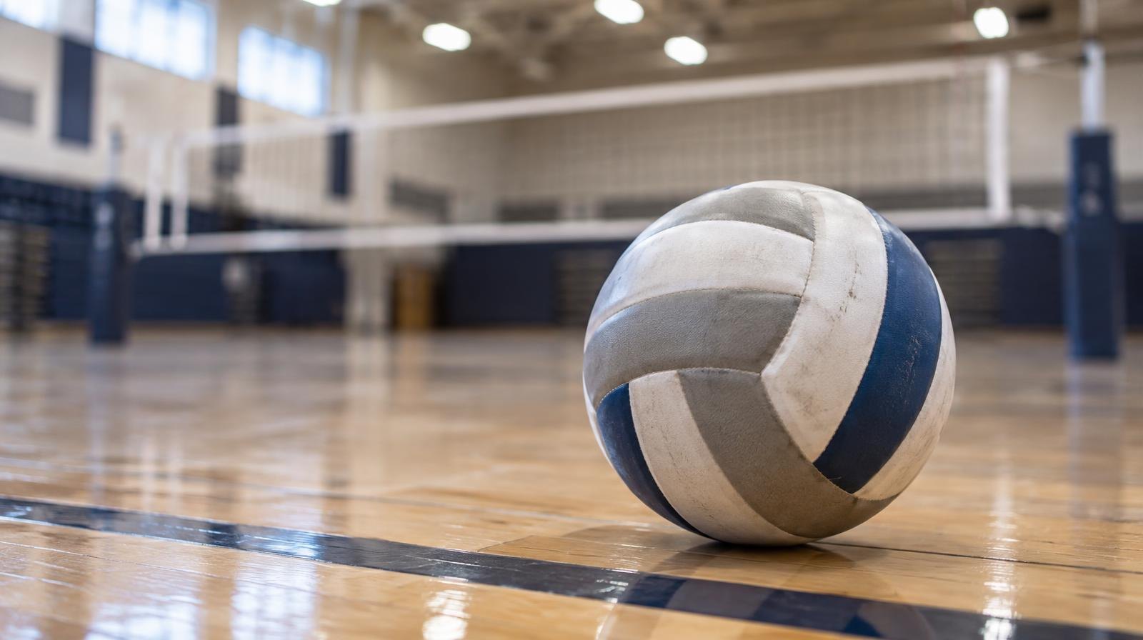 A volleyball resting on a hardwood gymnasium floor near a net.
