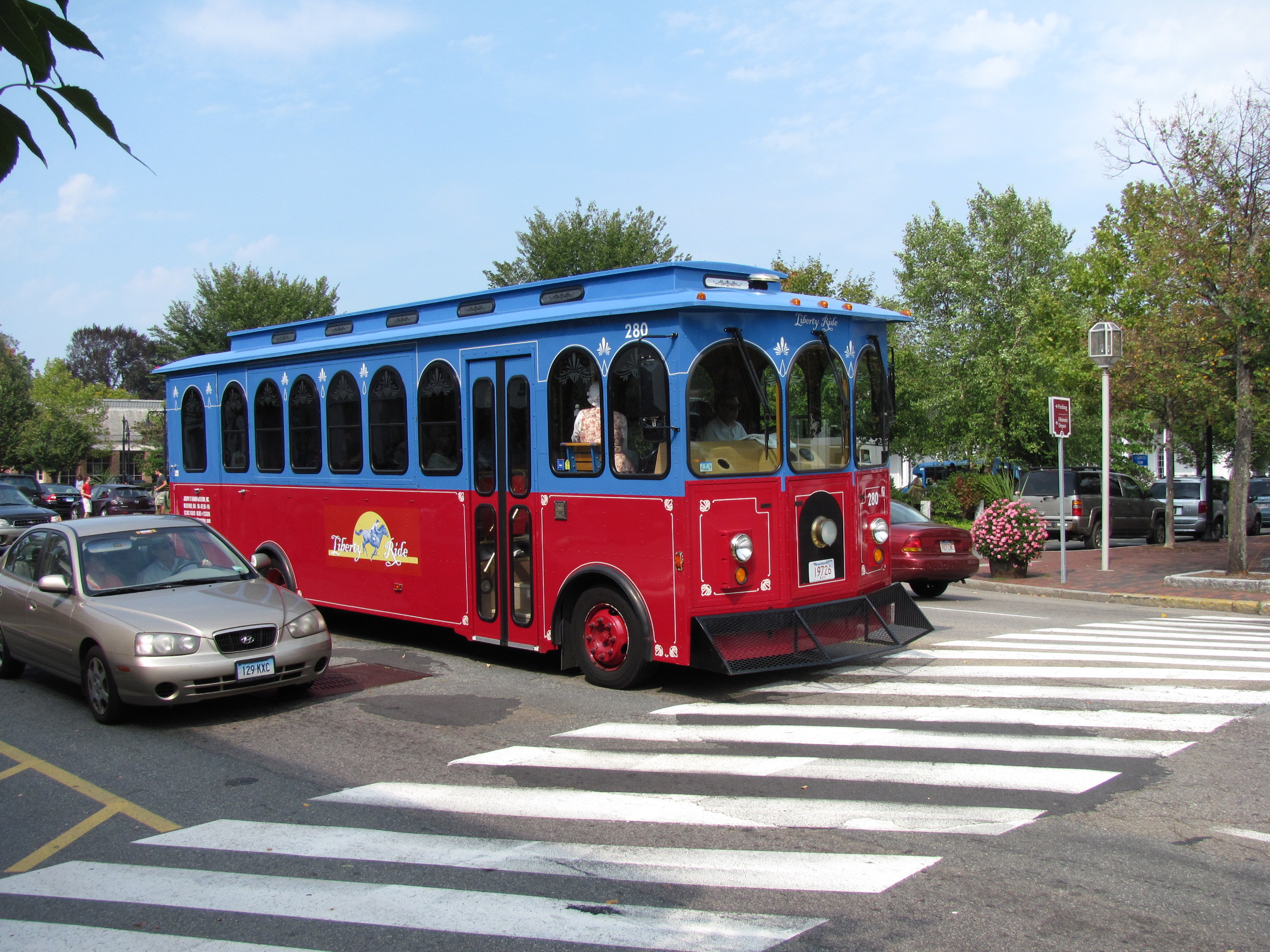 Red and blue Liberty Ride trolley bus crossing a suburban intersection.