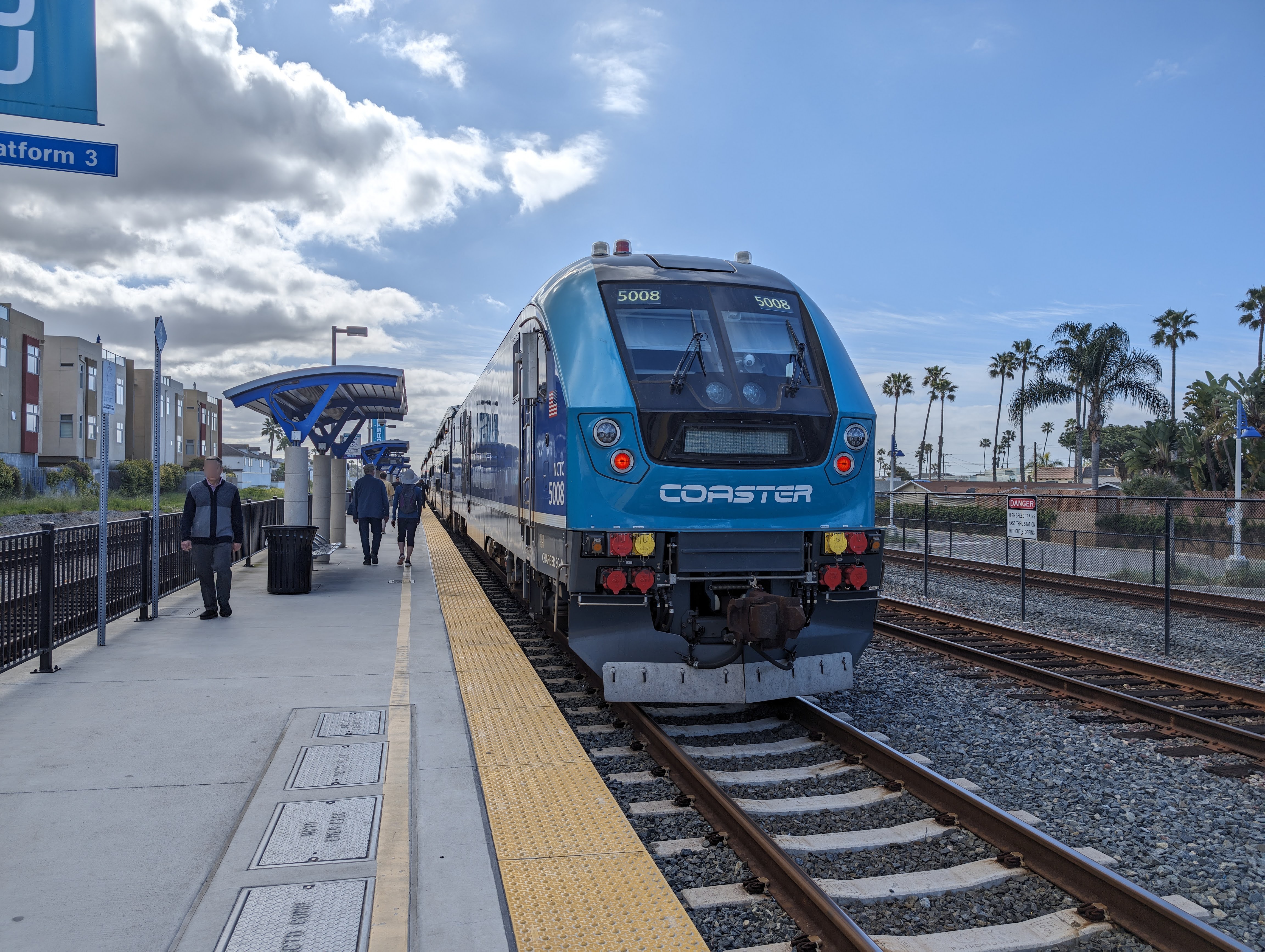 A blue COASTER commuter train stopped at a station platform with passengers nearby.