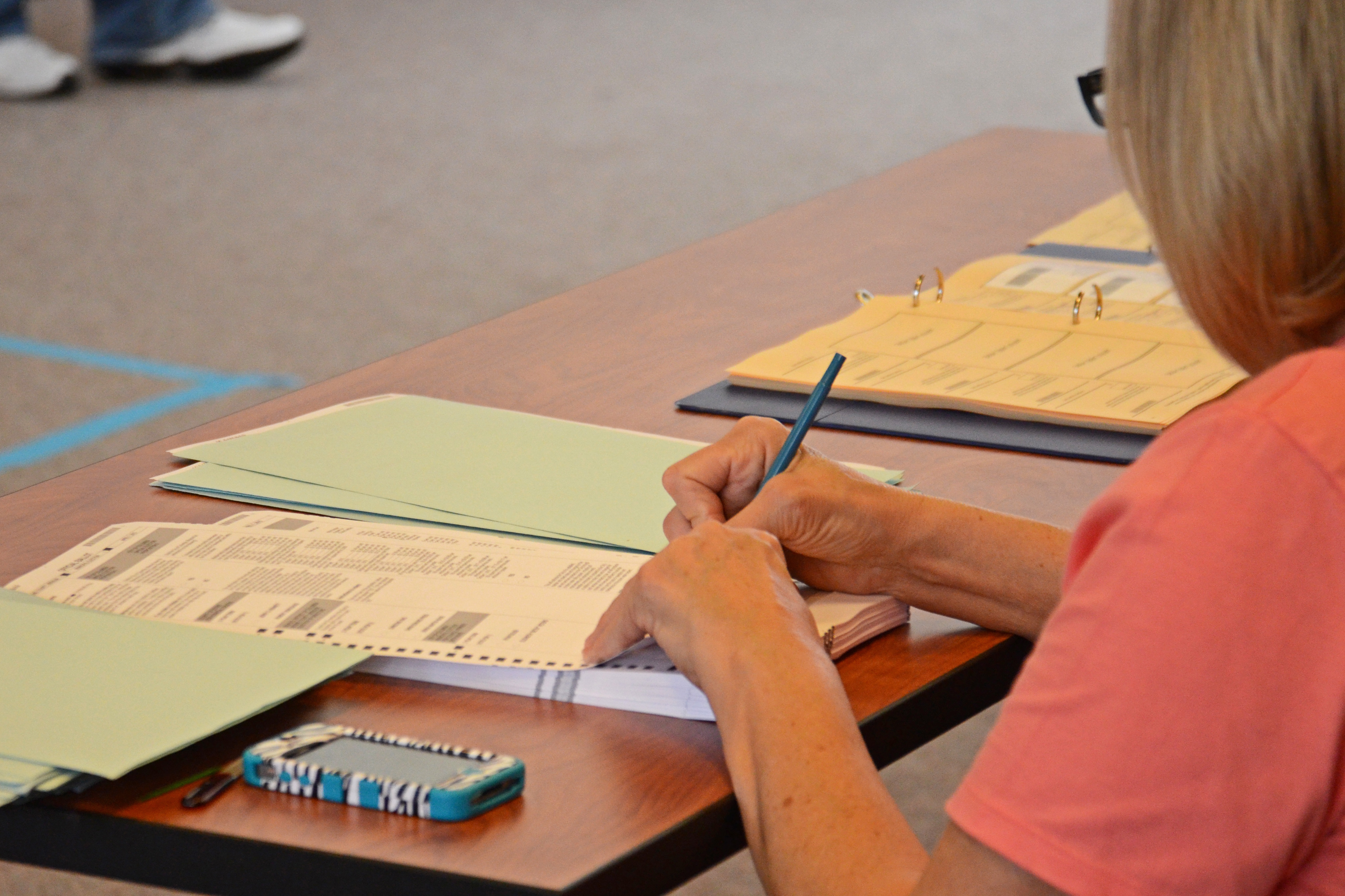 A person writing on election ballots spread across a table at a polling precinct.