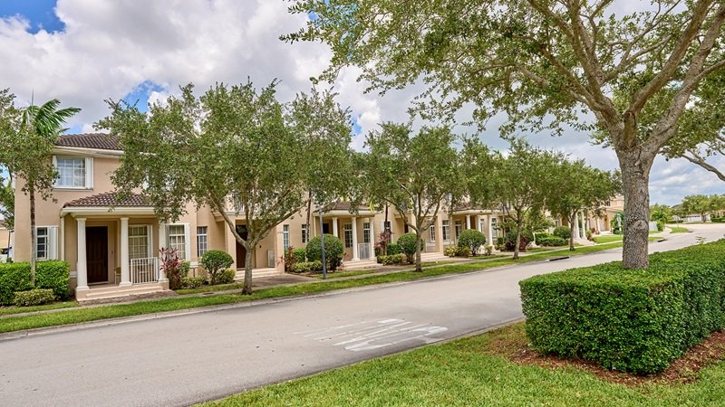 A tree-lined street fronting a row of two-story stucco townhomes with tile roofs.