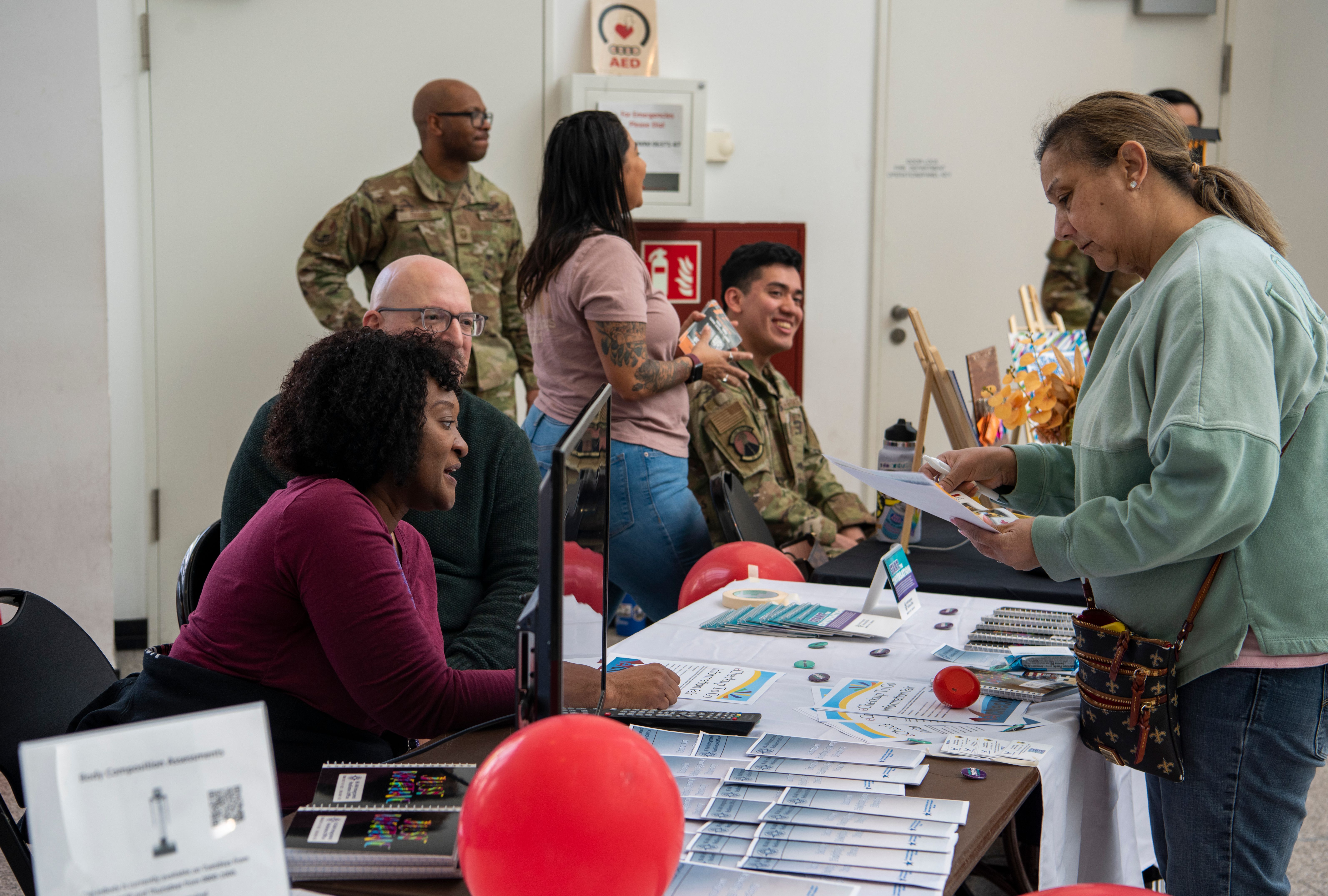 People browse brochures and speak with representatives at tables inside an indoor resource fair.